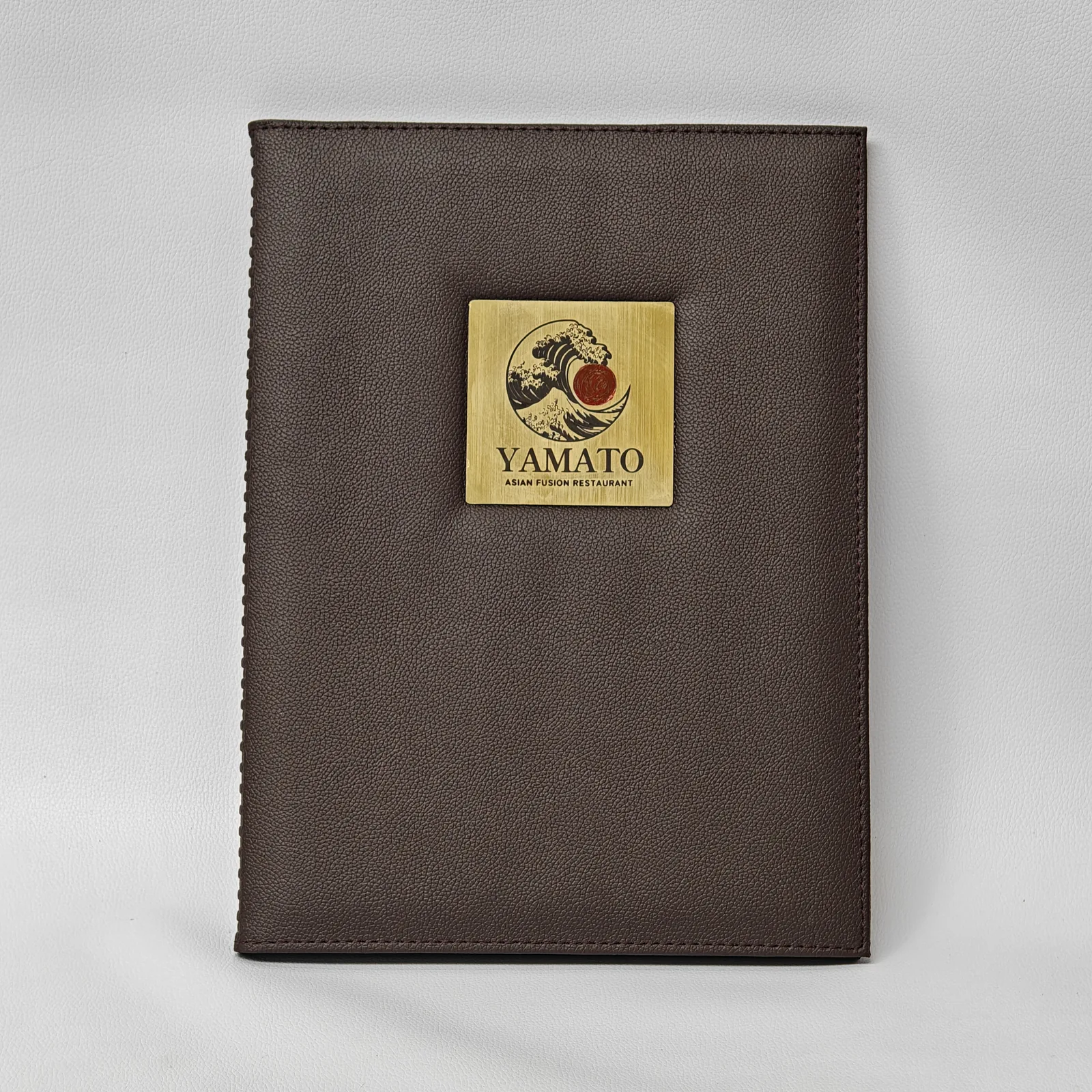 Front view of a brown pebbled leather menu cover with a square metal logo plate in the center.