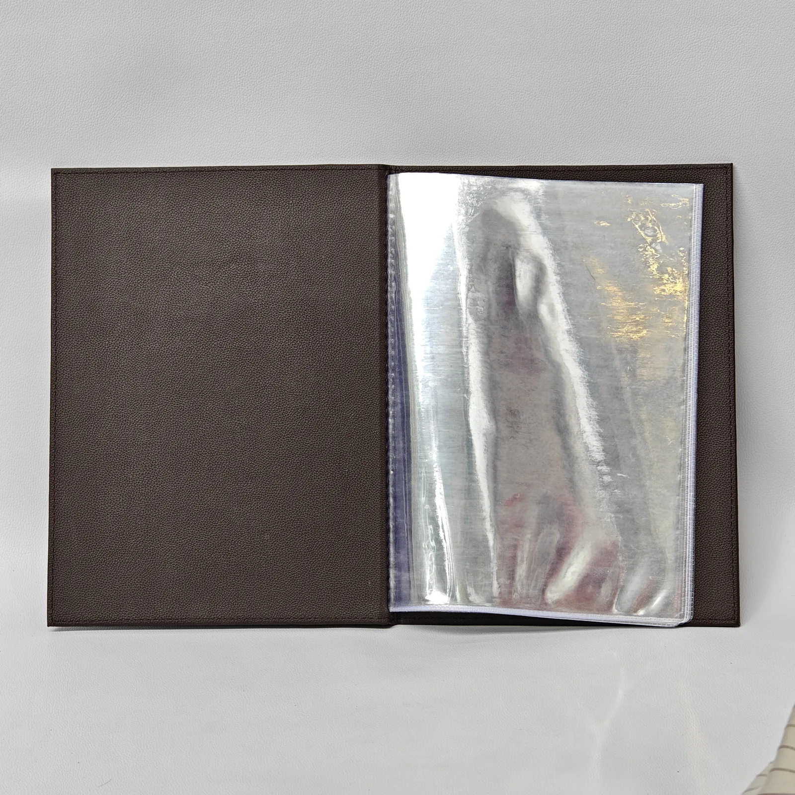 Open view of a brown leather menu cover showing clear plastic sleeves for holding menu pages.