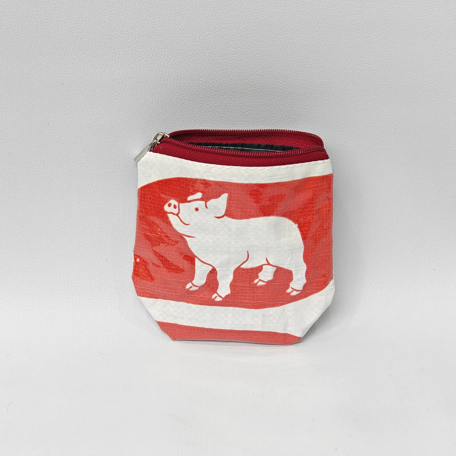 Red pig-print handmade pouch with maroon zipper showing traditional illustration style