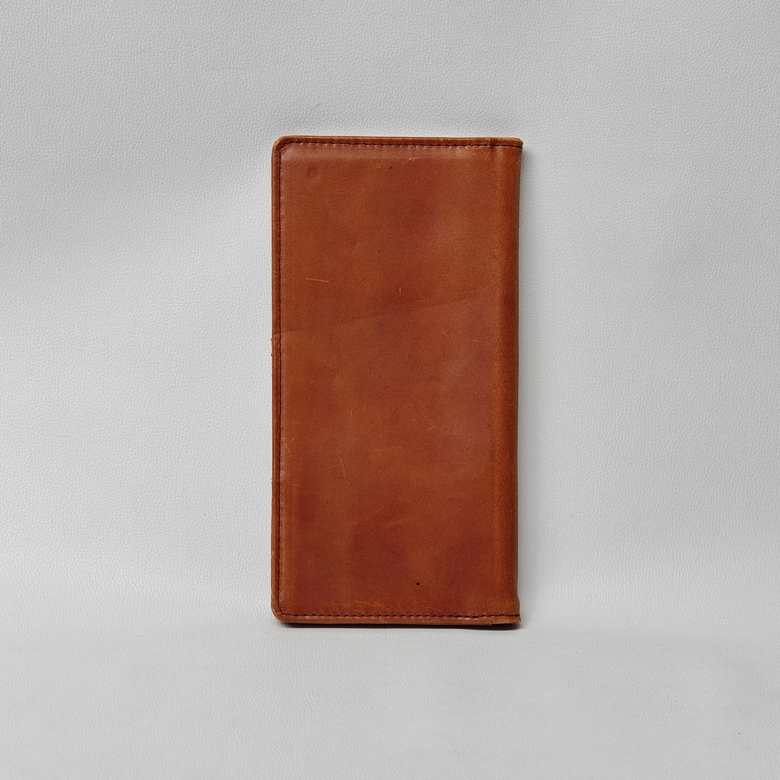 Plain back view of a closed brown leather check presenter with visible perimeter stitching.