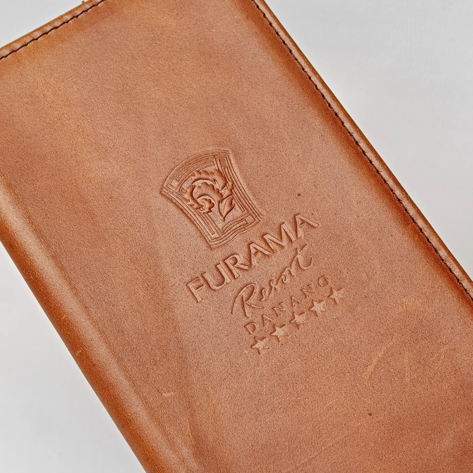 Close-up of a debossed logo and text on the surface of brown leather.