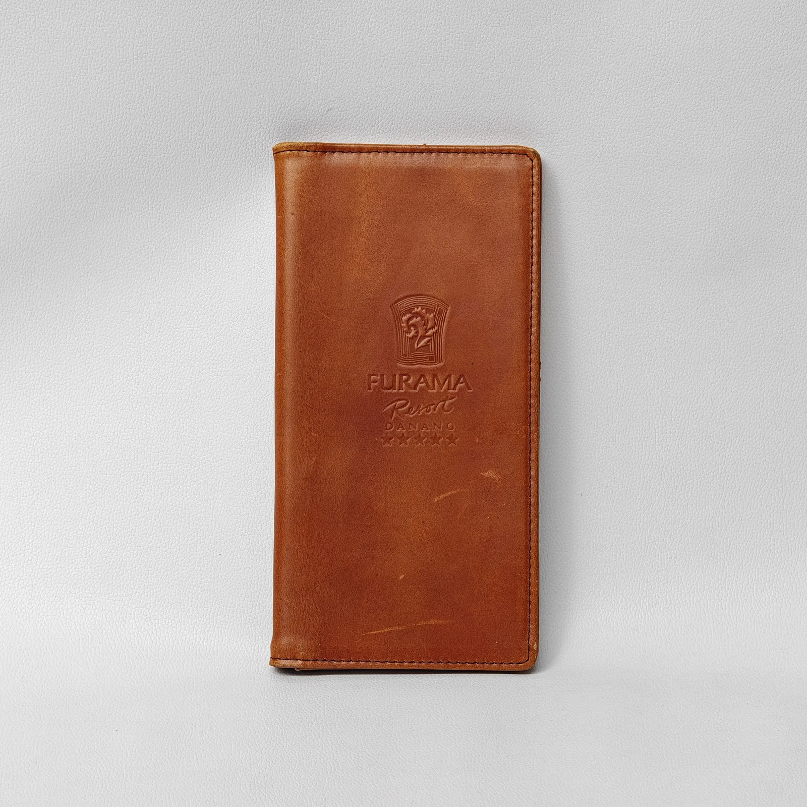Front view of a closed brown leather check presenter with a debossed logo and perimeter stitching.