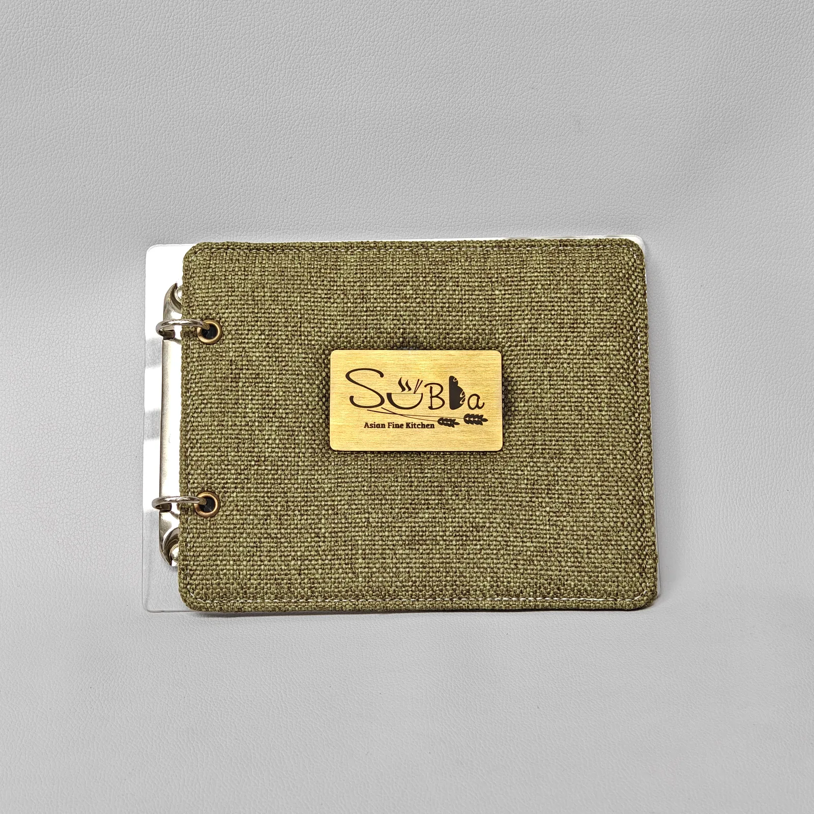 Front view of an olive green woven canvas menu cover with a rectangular metal plate and two-ring binding.