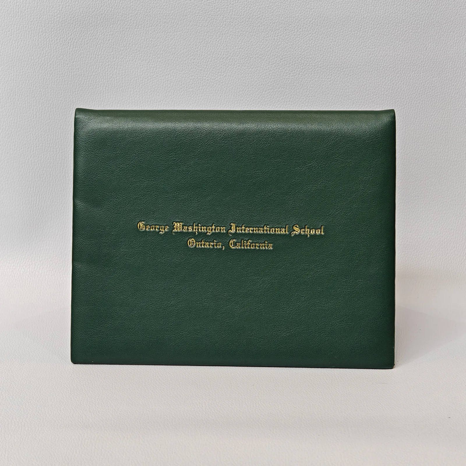 Forest green leather certificate cover with gold foil embossed branding and yellow bookmark accent