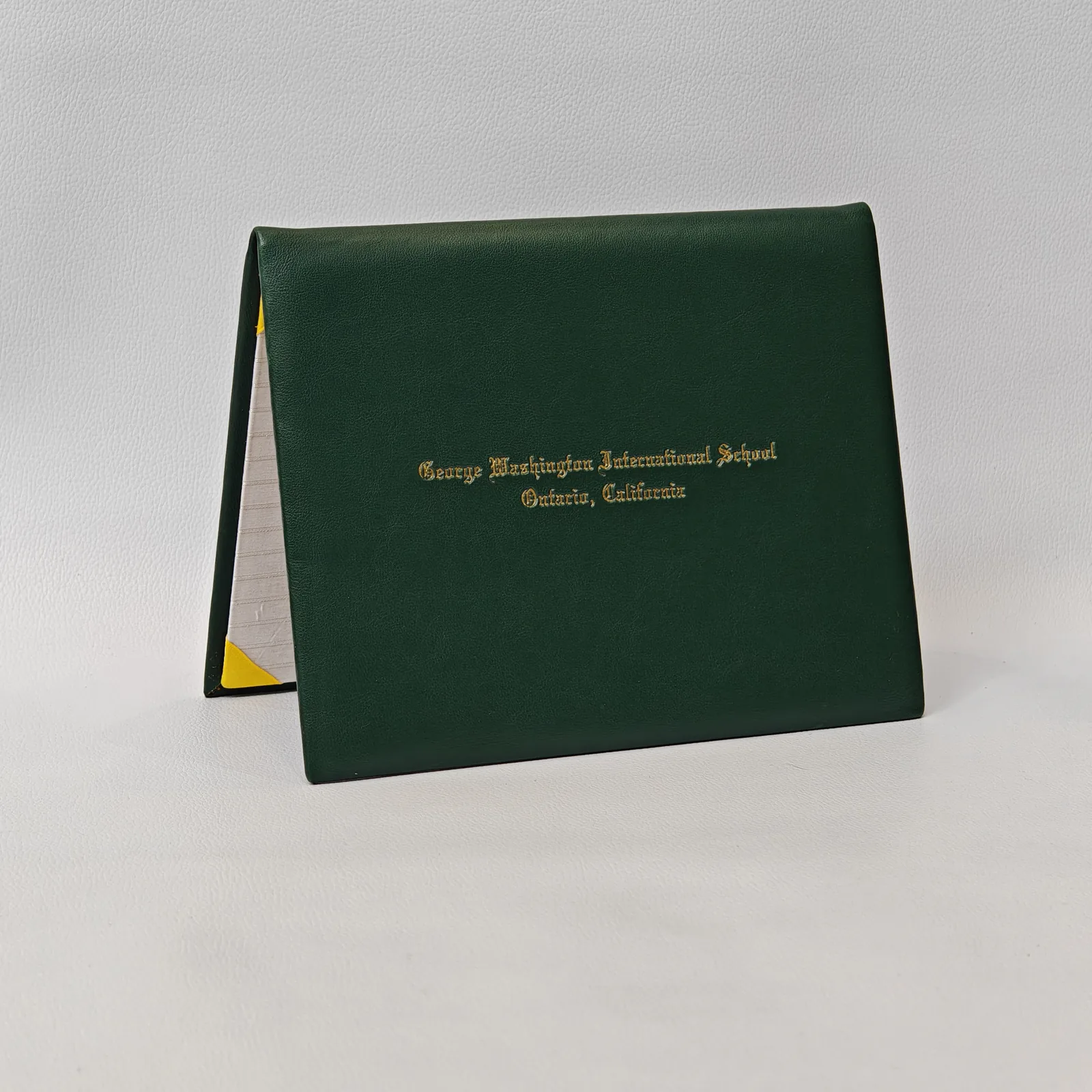 Open leather certificate cover showing book binding, metal rings, and yellow fabric detail