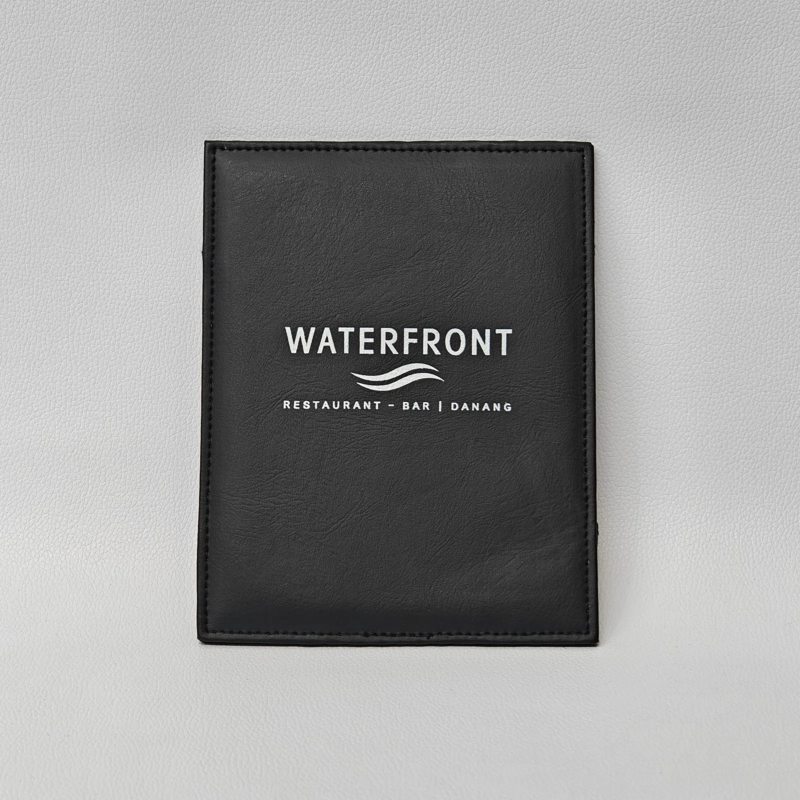 Black leather bill presenter with embossed restaurant branding and diamond corner details