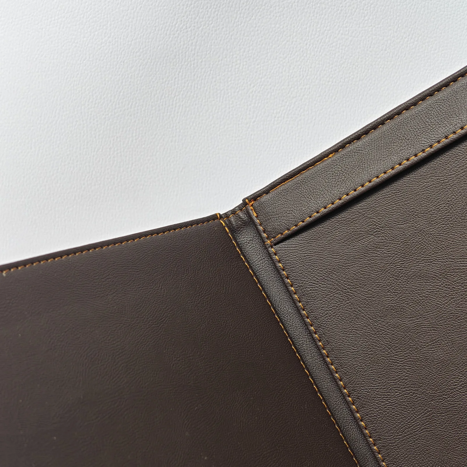 Close-up of the stitched hinge on a dark brown leather folder.