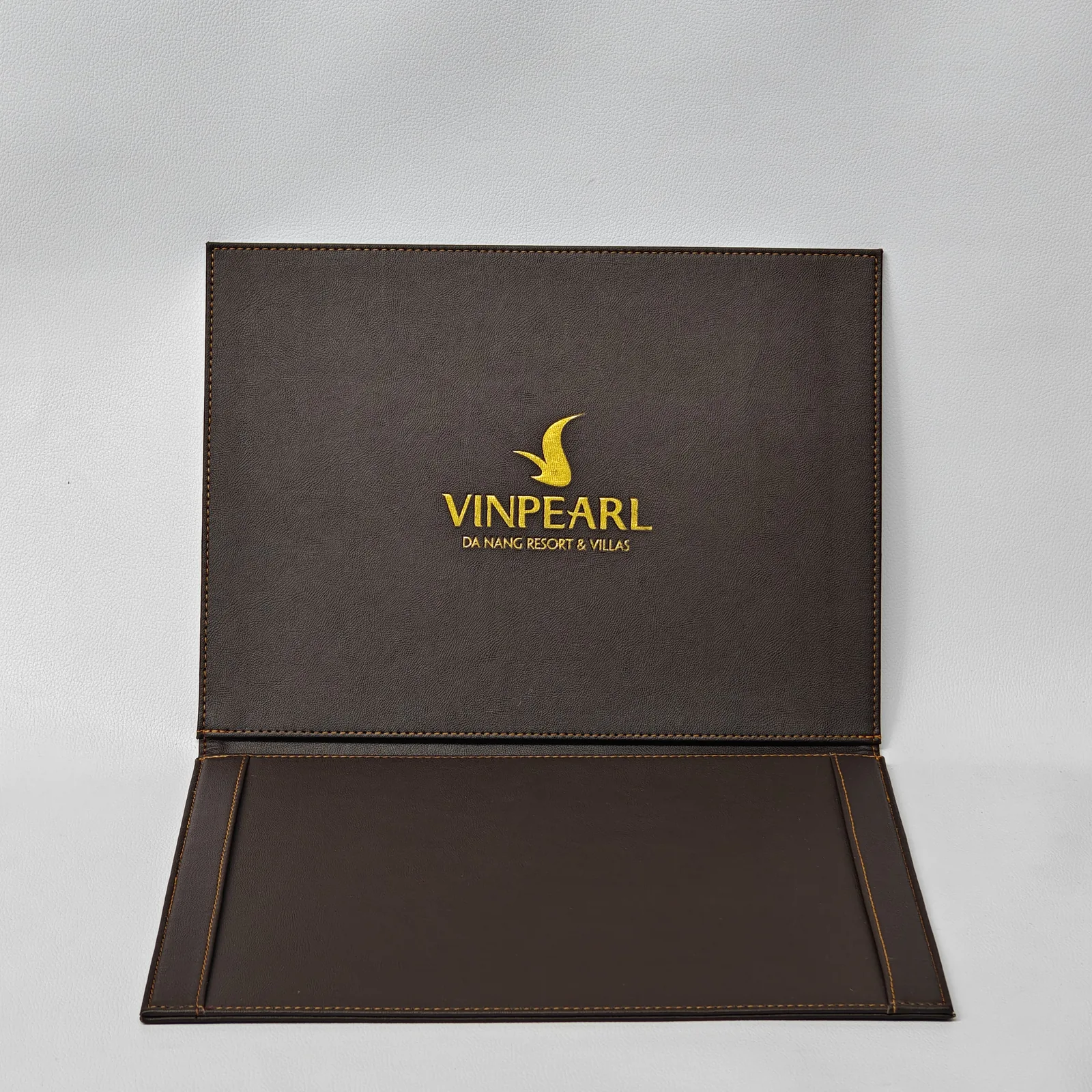 Open dark brown leather folder with an interior pocket and a gold logo on the inside cover.