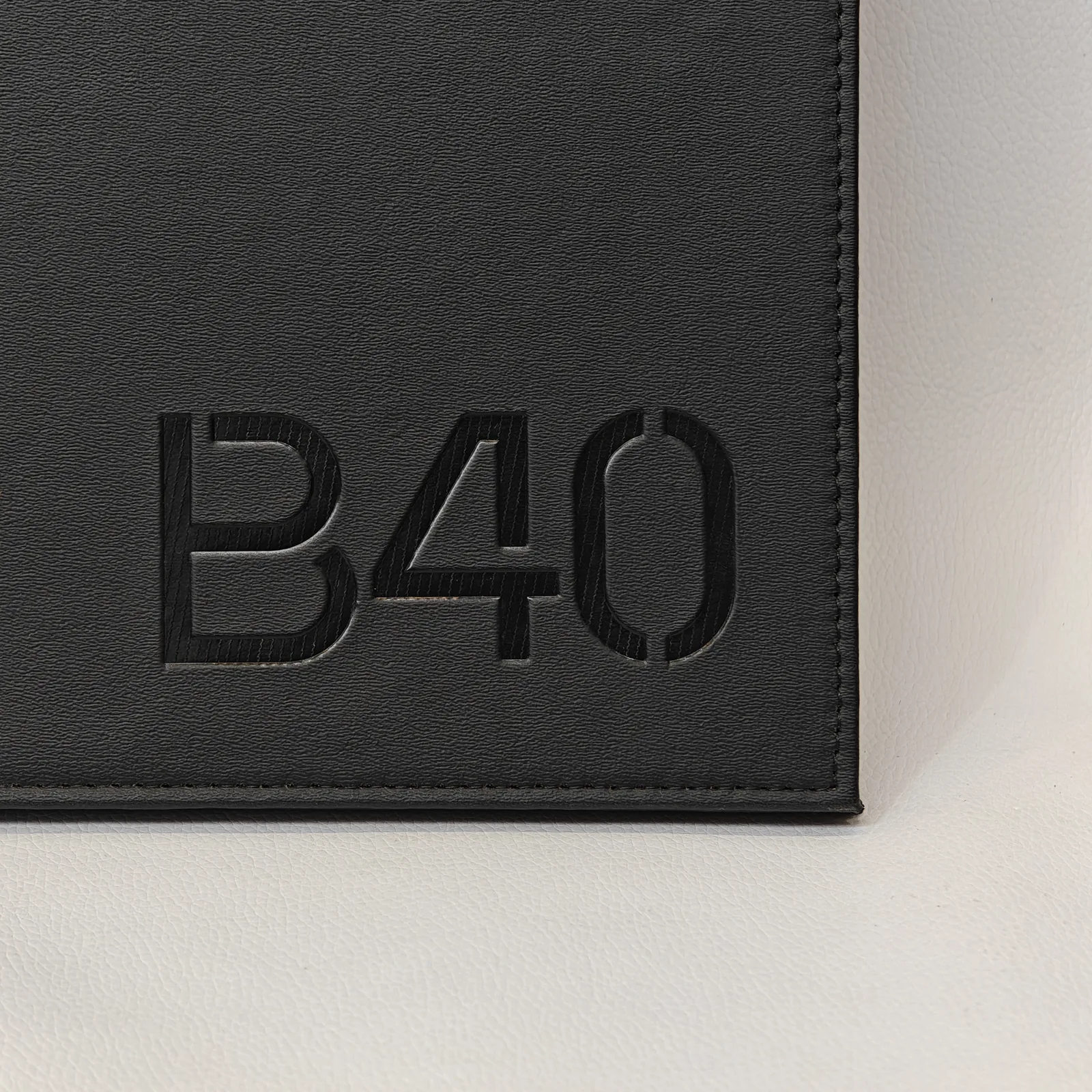 Close-up of debossed alphanumeric characters and fine perimeter stitching on a black textured leather surface.