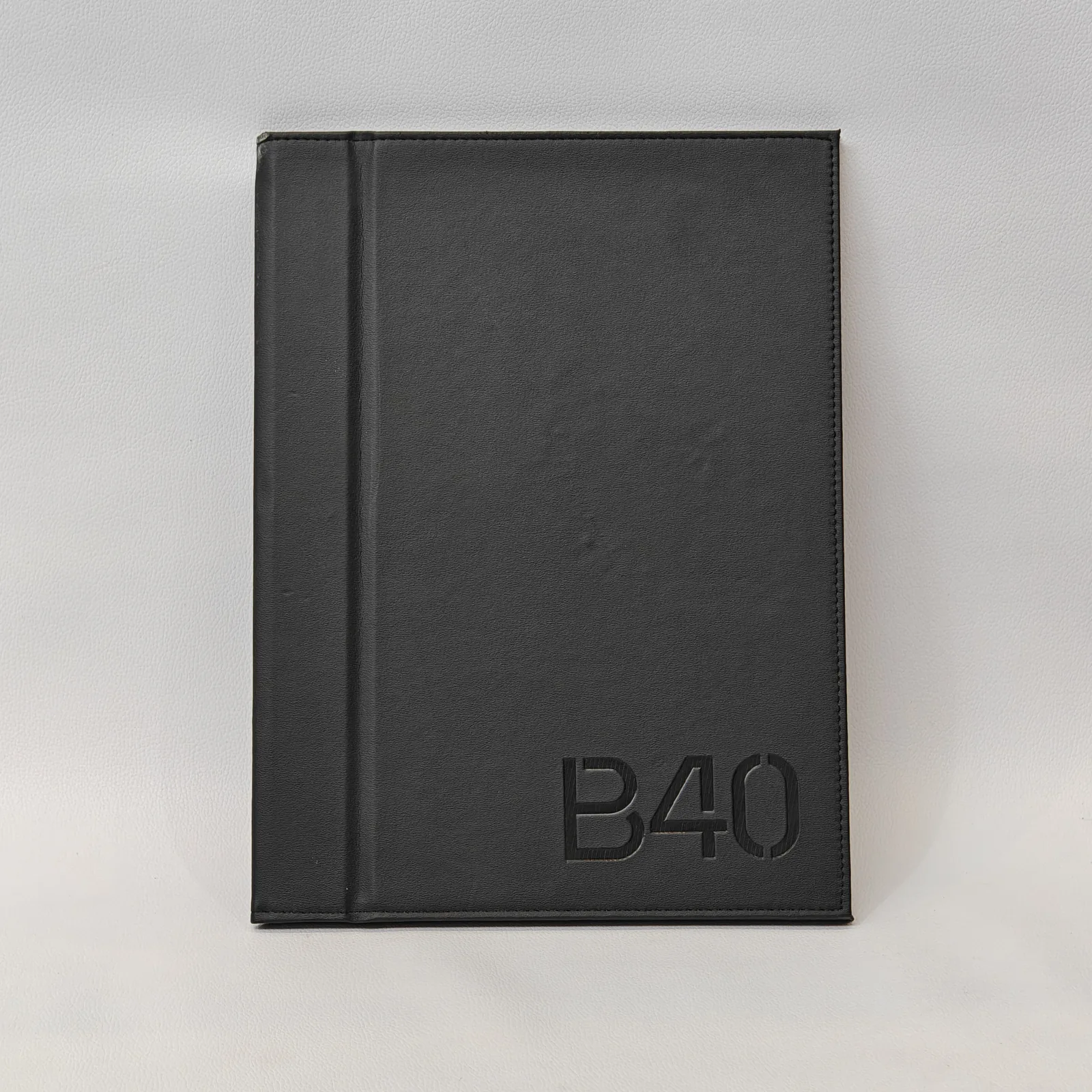 Front view of a black textured leather menu cover with debossed characters and perimeter stitching.