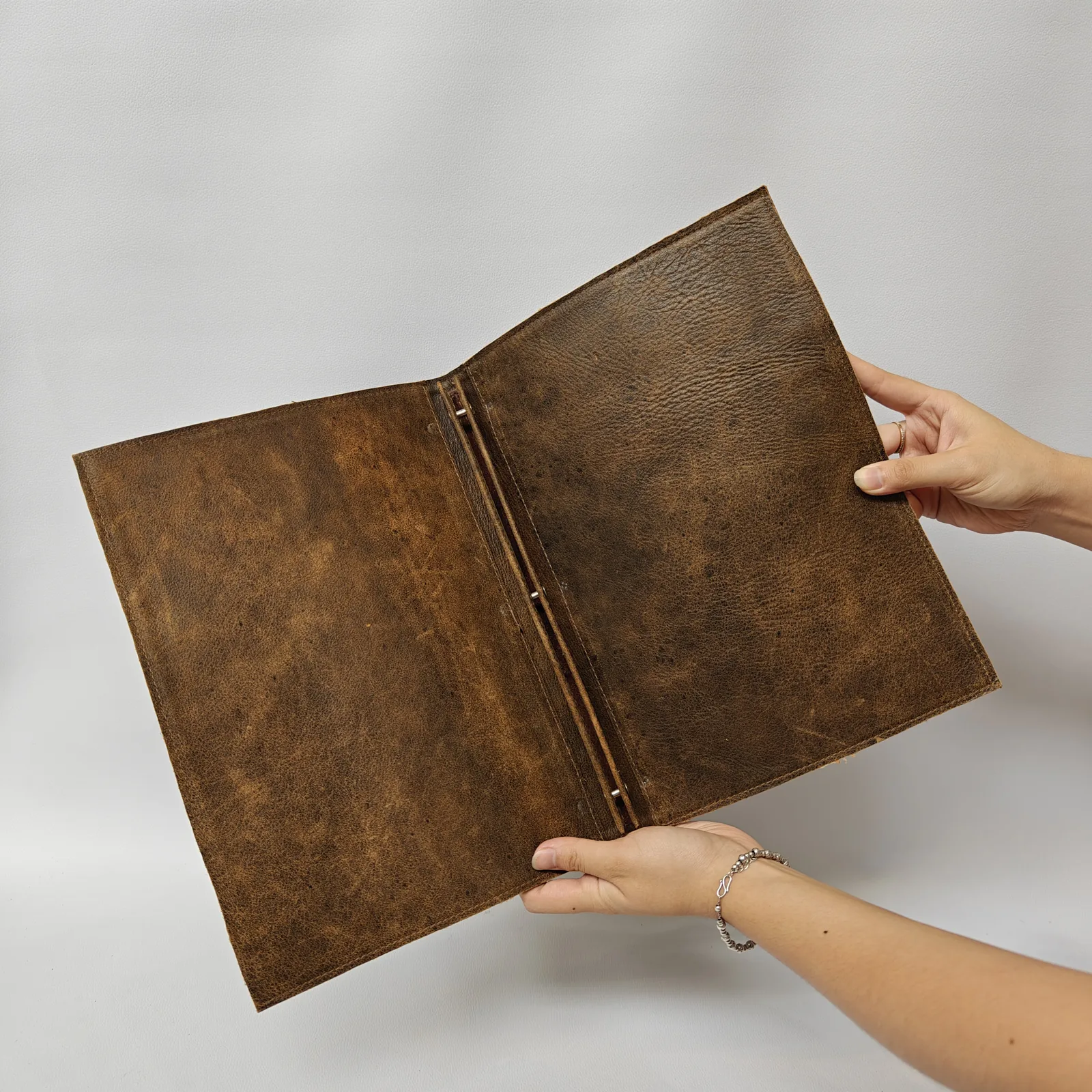 Interior of an open brown leather menu cover held by hands, showing the screw post binding system.