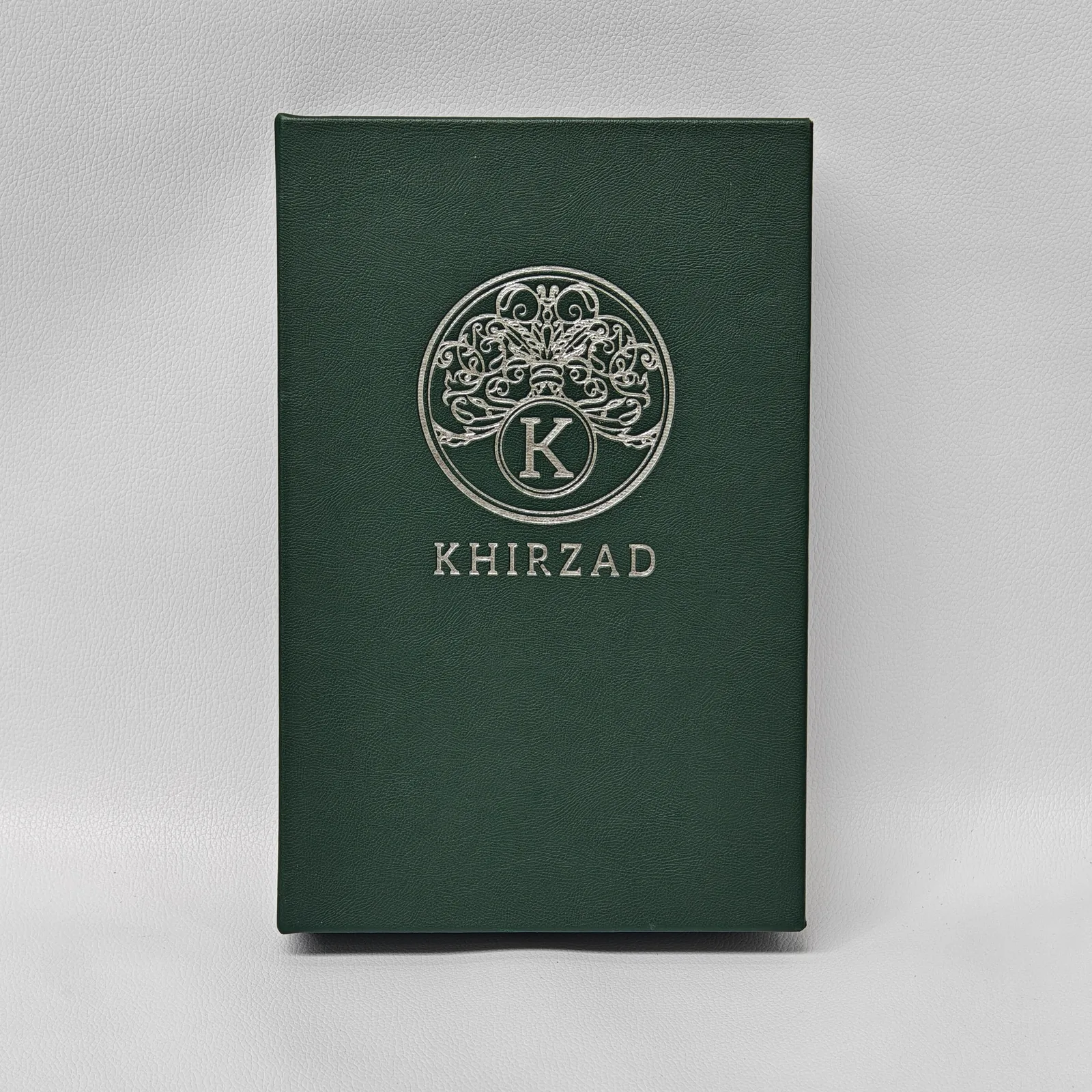 Deep green pebbled leather book cover with ornate gold foil logo