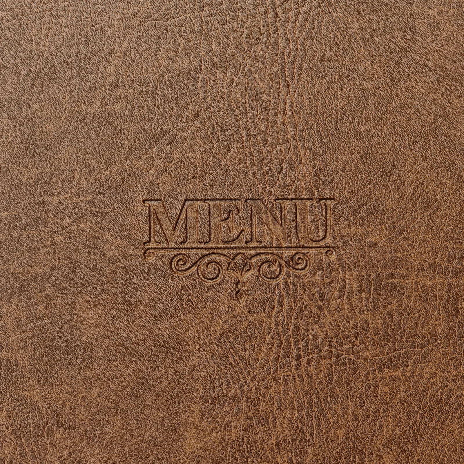 Close-up of debossed MENU text and scrollwork on brown textured material.