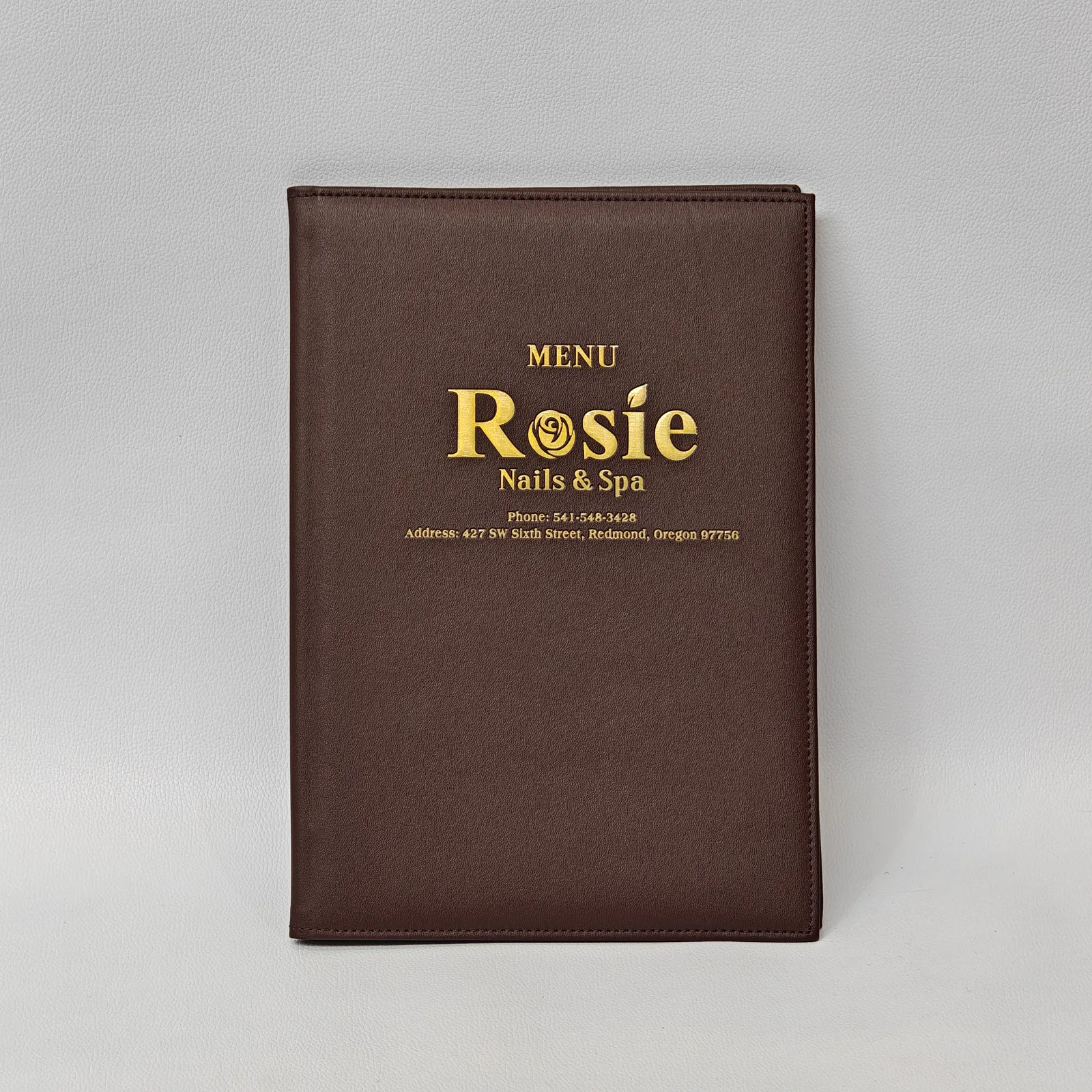 Closed brown leather menu cover with gold foil lettering and perimeter stitching.