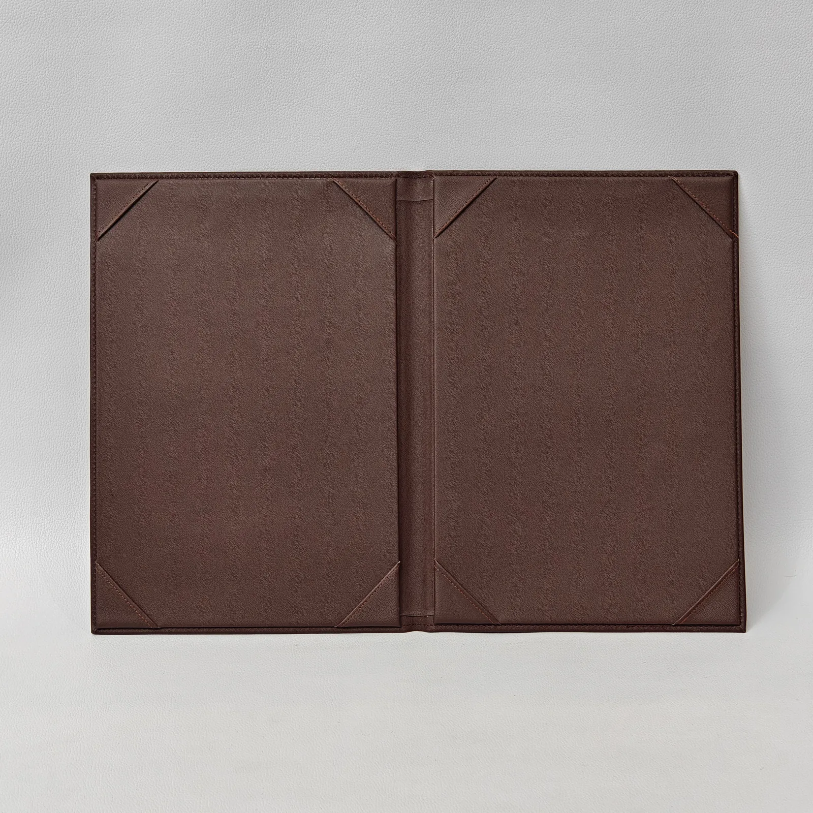 Open brown leather menu cover showing two panels with triangular corner pockets for holding pages.