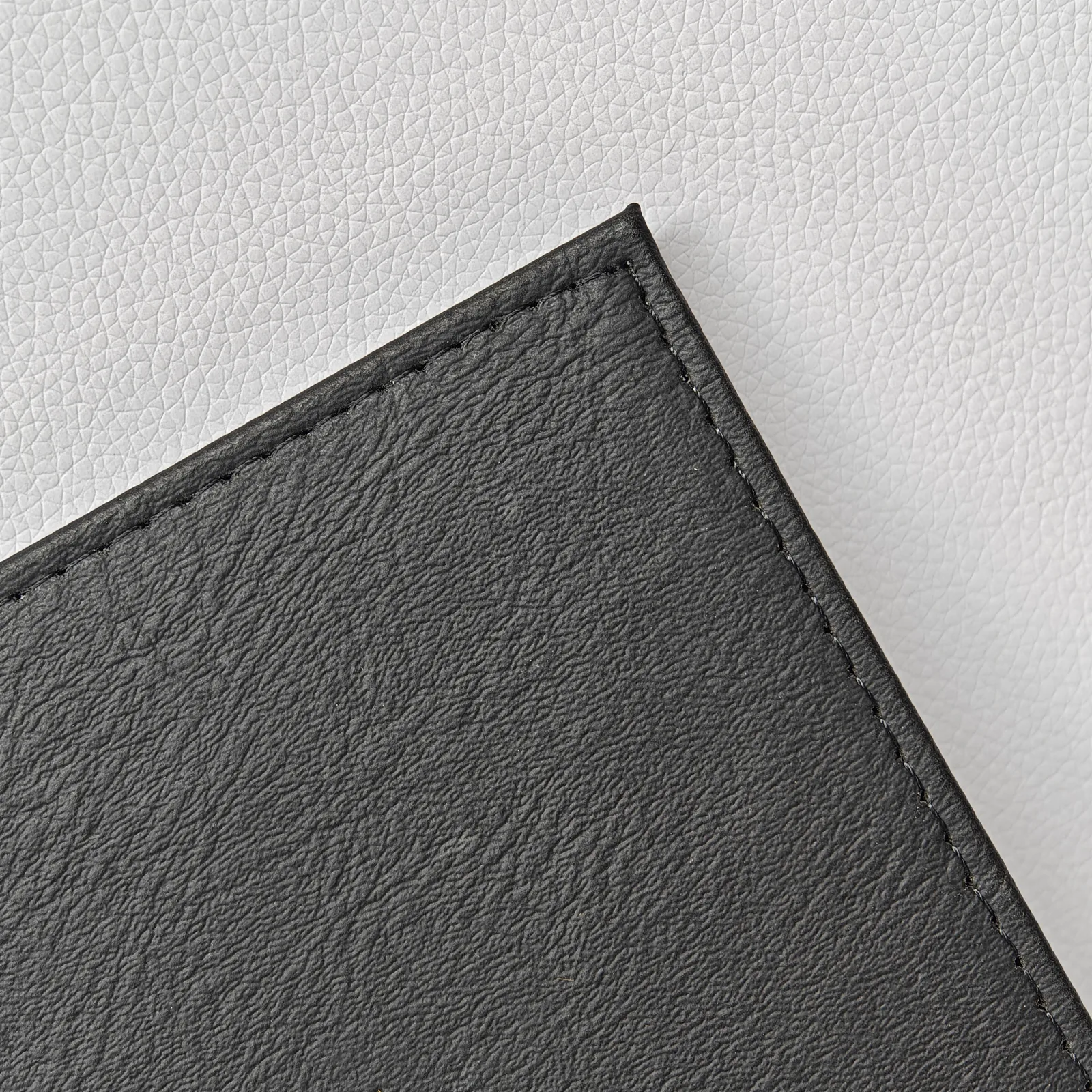 Close-up of the corner of a black leather menu cover showing fine perimeter stitching and pebbled texture.