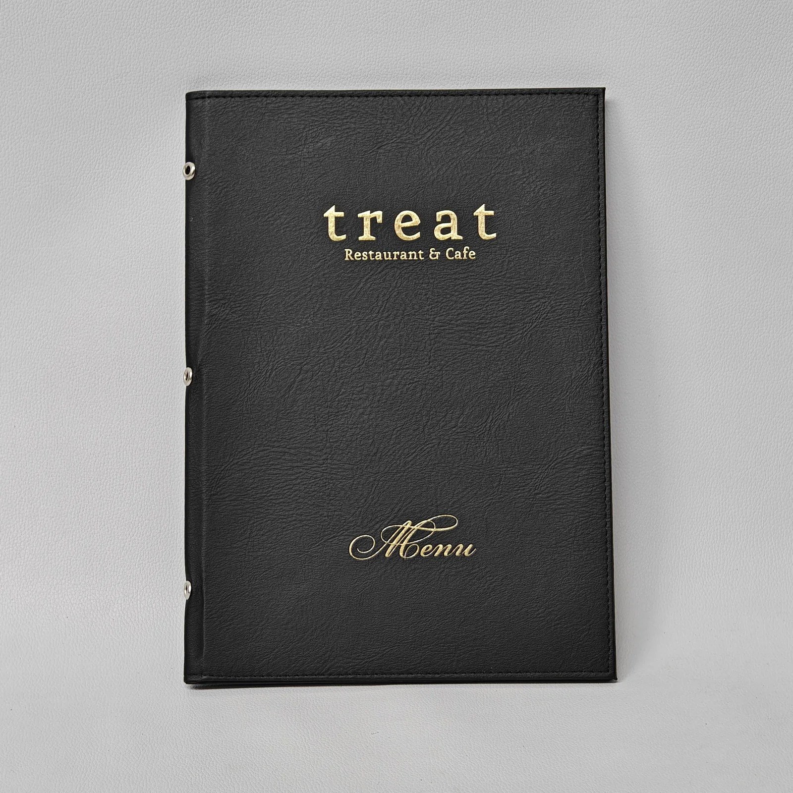 Closed black textured leather menu cover with gold foil lettering and three silver grommets on the spine.