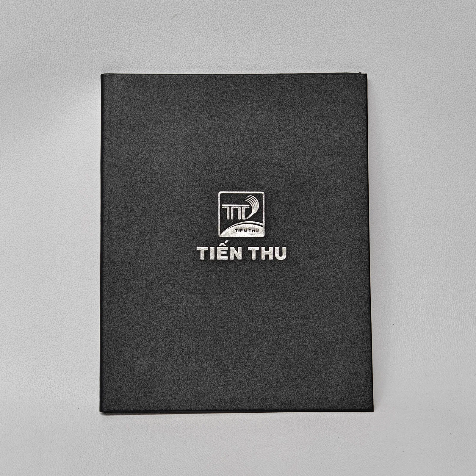 Front of a black pebbled leather folder with a silver logo and text.