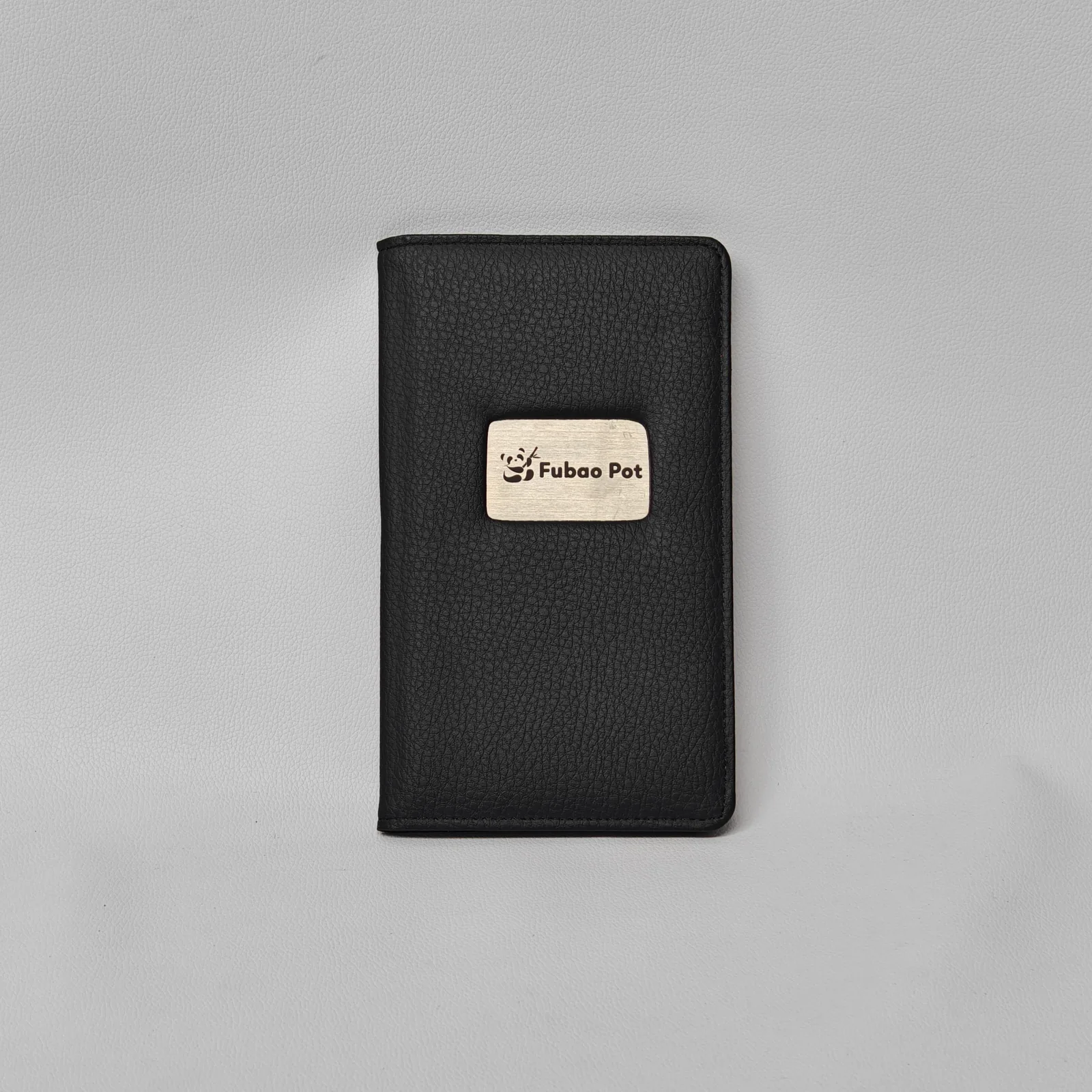 Front view of a black pebbled leather check presenter with a central metal logo plate.