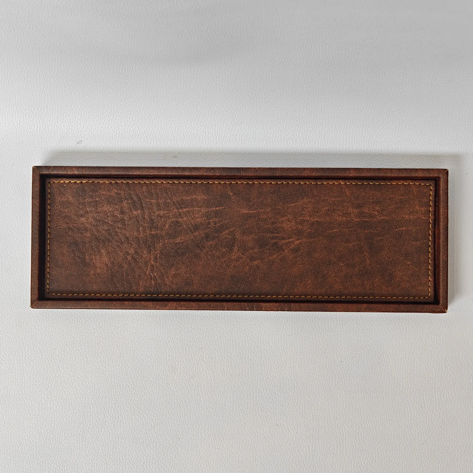 A top-down view of a rectangular brown leather tray showing its textured surface and interior stitching.
