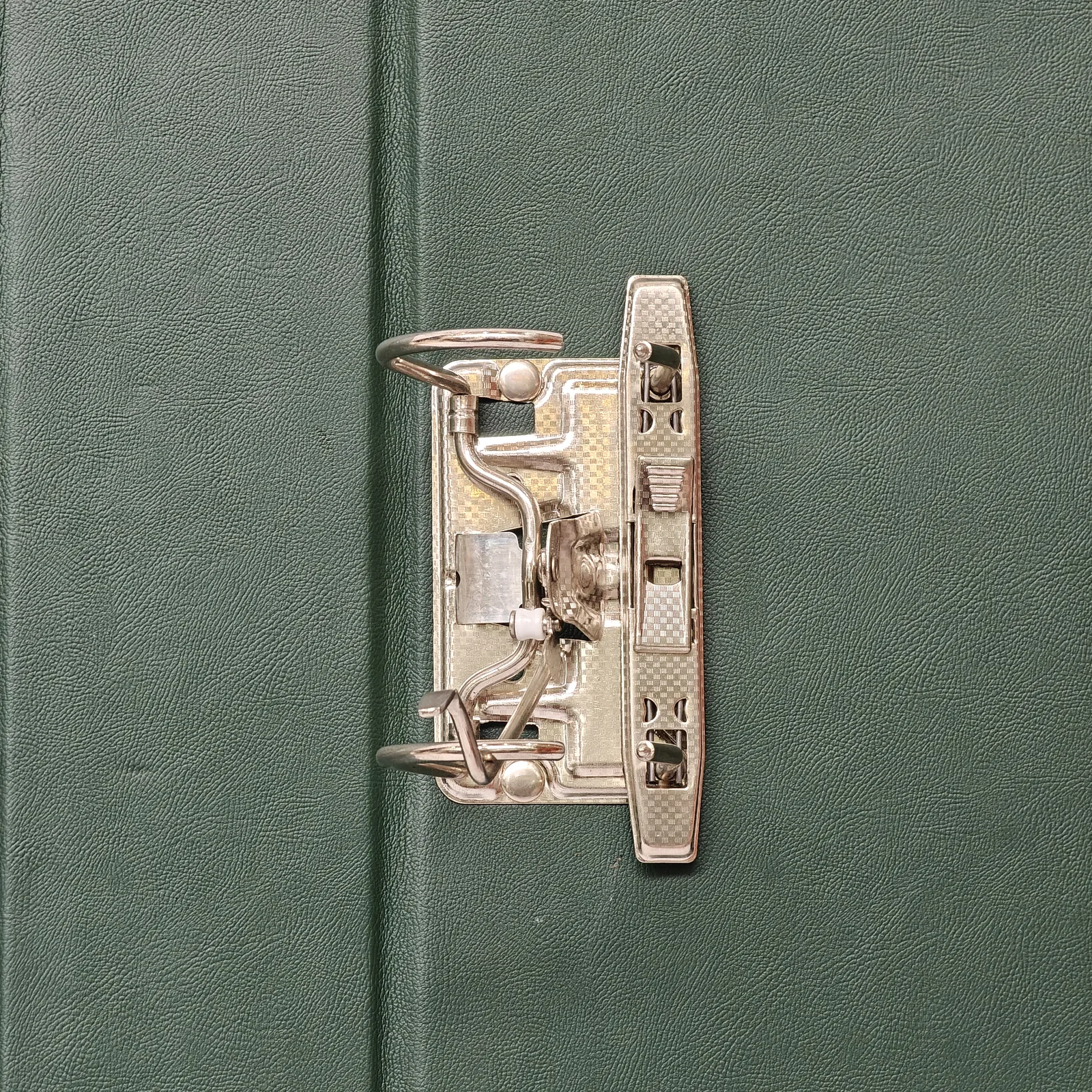 Close-up of the silver metal lever arch ring mechanism on a green textured surface.