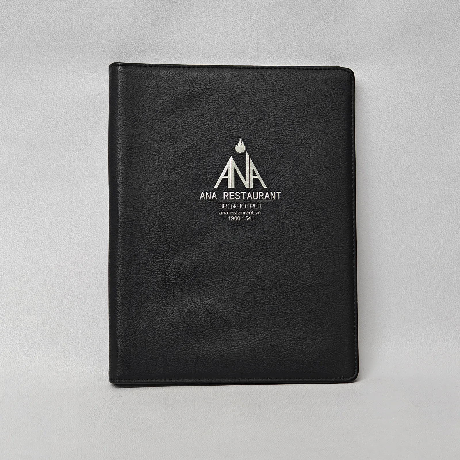 Black textured leather menu cover with silver foil logo and perimeter stitching.