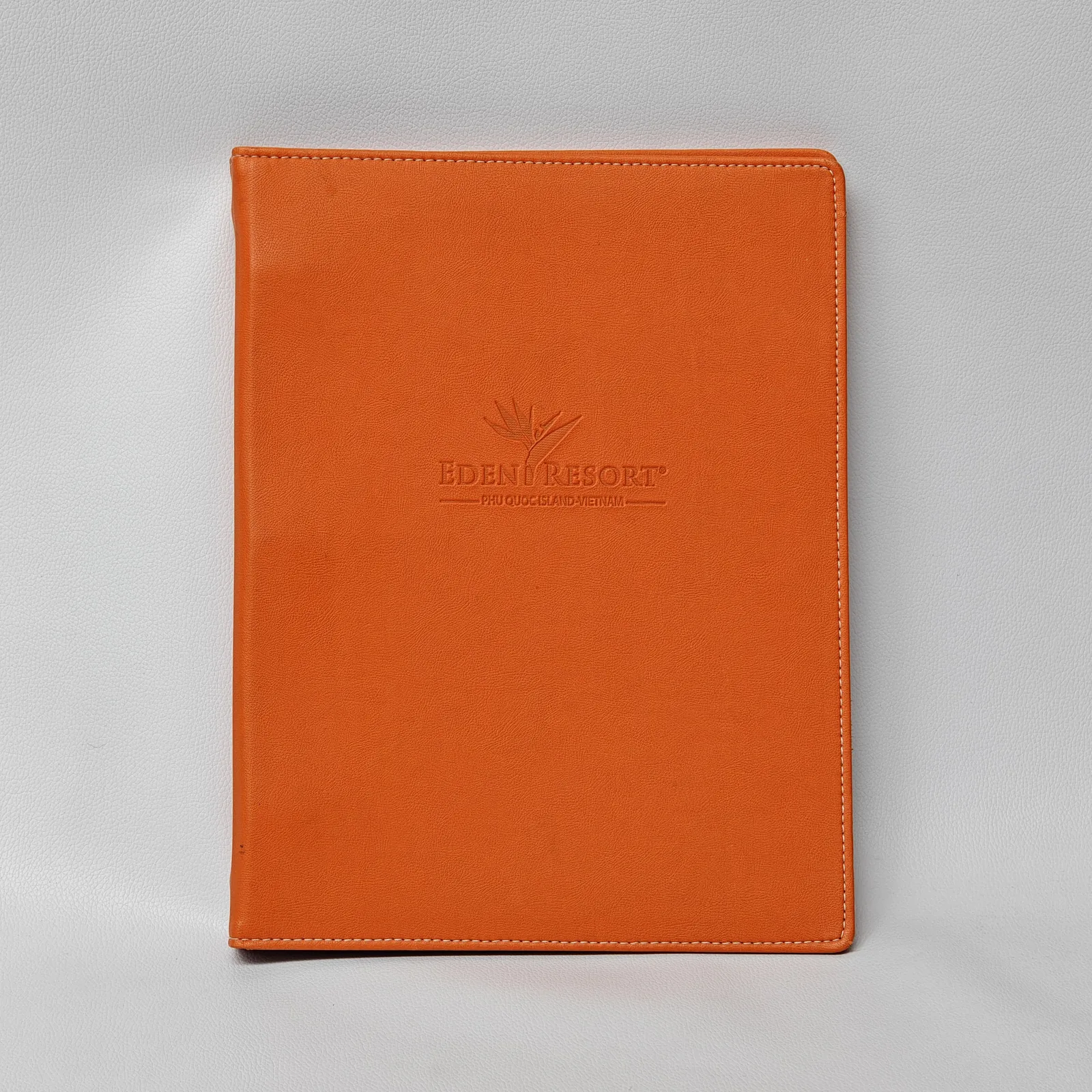 Closed orange leather binder with debossed logo and white contrast stitching.