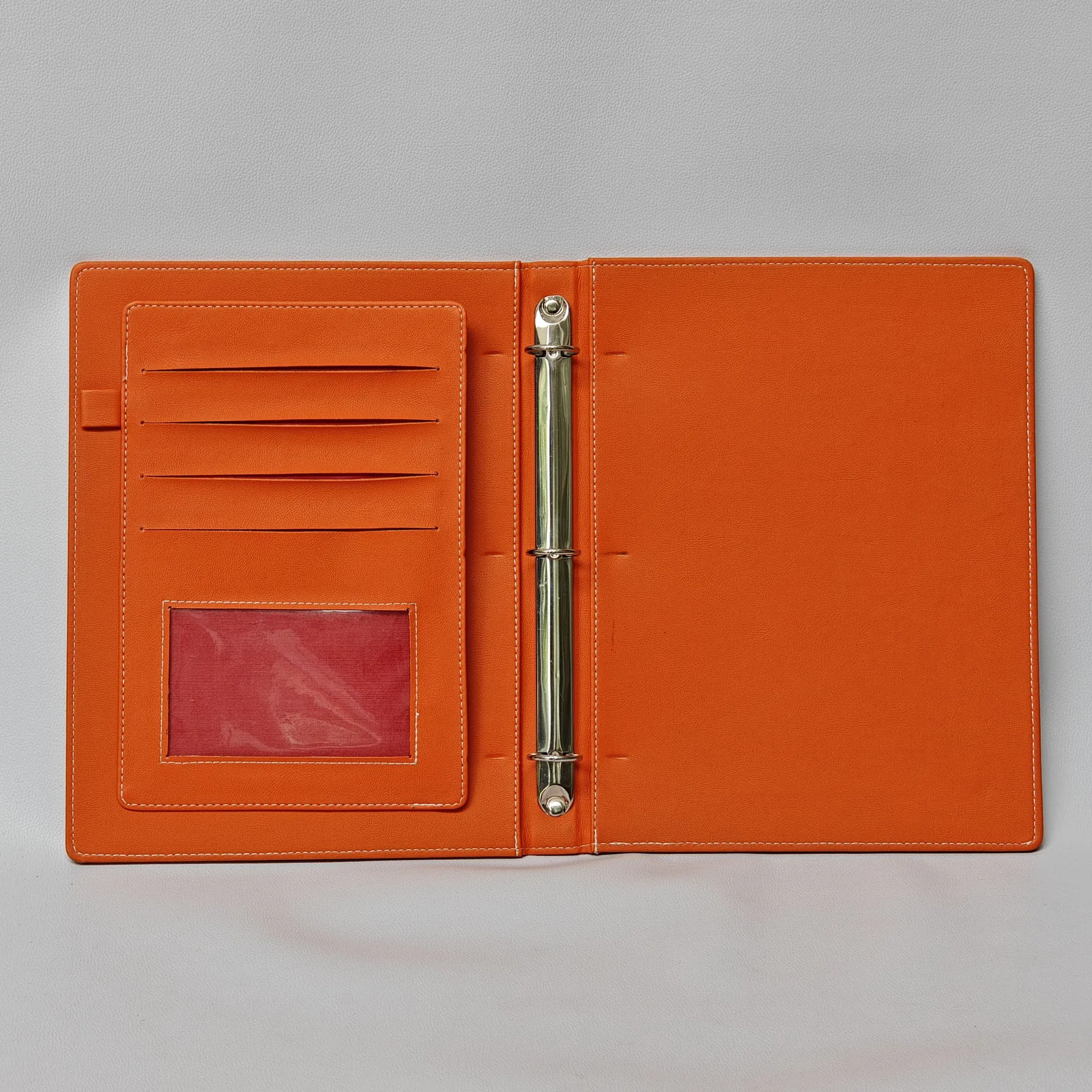 Interior of an orange leather binder featuring a silver three-ring mechanism and multiple card pockets.