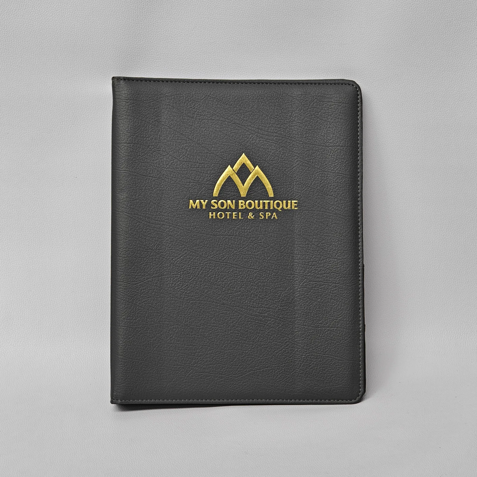 Front view of a black textured leather binder with a gold foil logo and perimeter stitching.