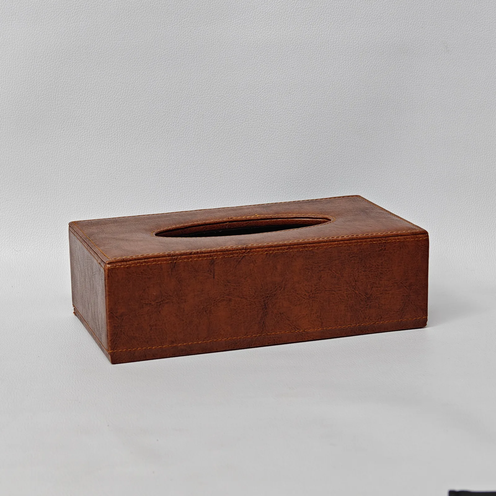 Angled view of a textured brown leather tissue box cover showing its rectangular shape and top opening.