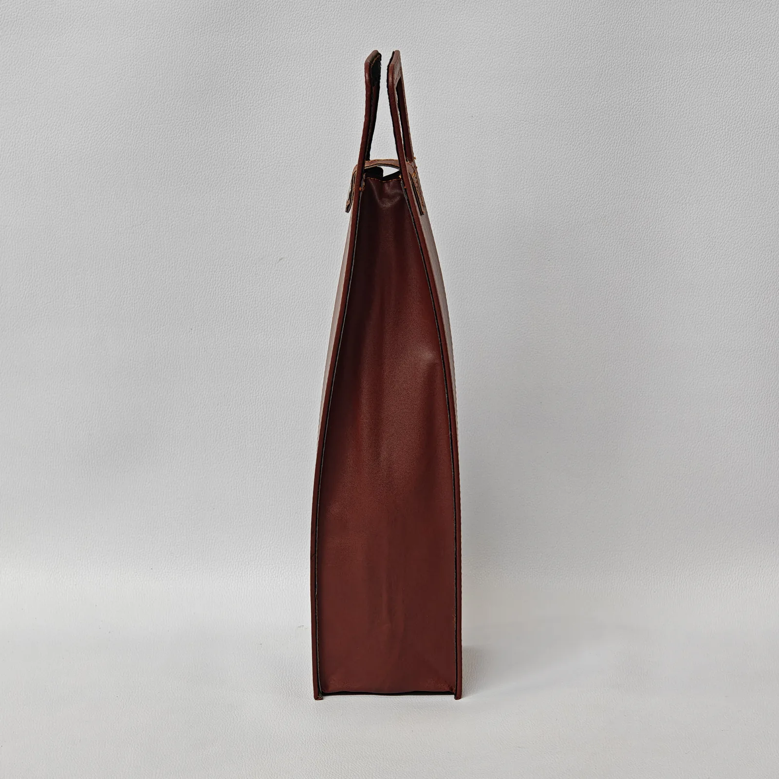 Side profile of a structured brown leather wine bottle carrier.