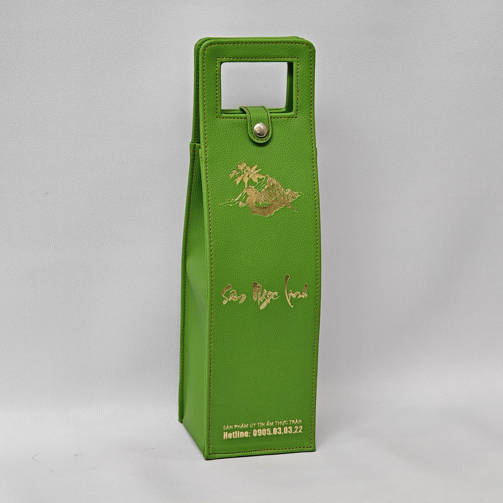 Angled view of a green pebbled leather wine carrier with gold foil branding.