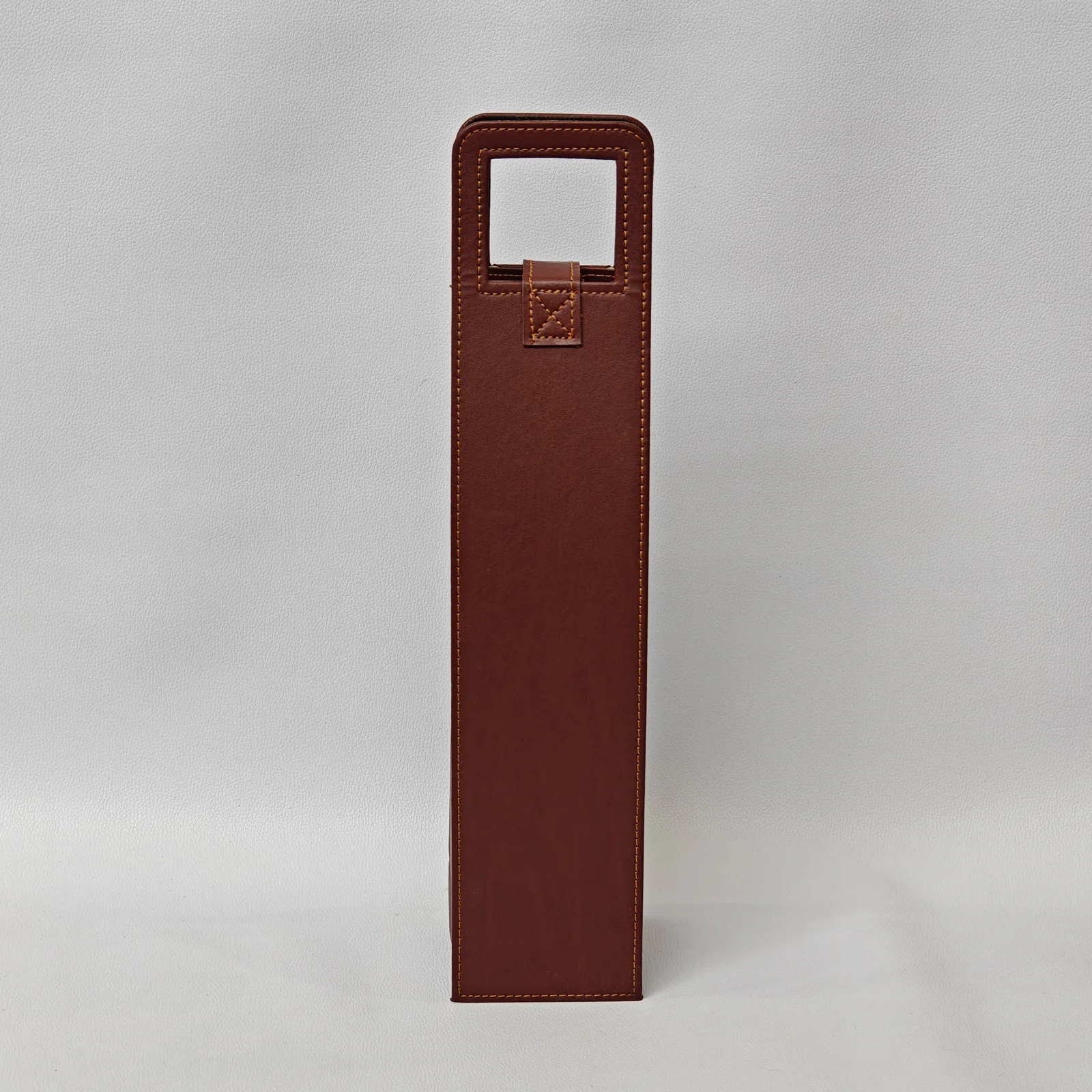 Back view of a brown leather wine bottle carrier showing the stitched handle attachment.
