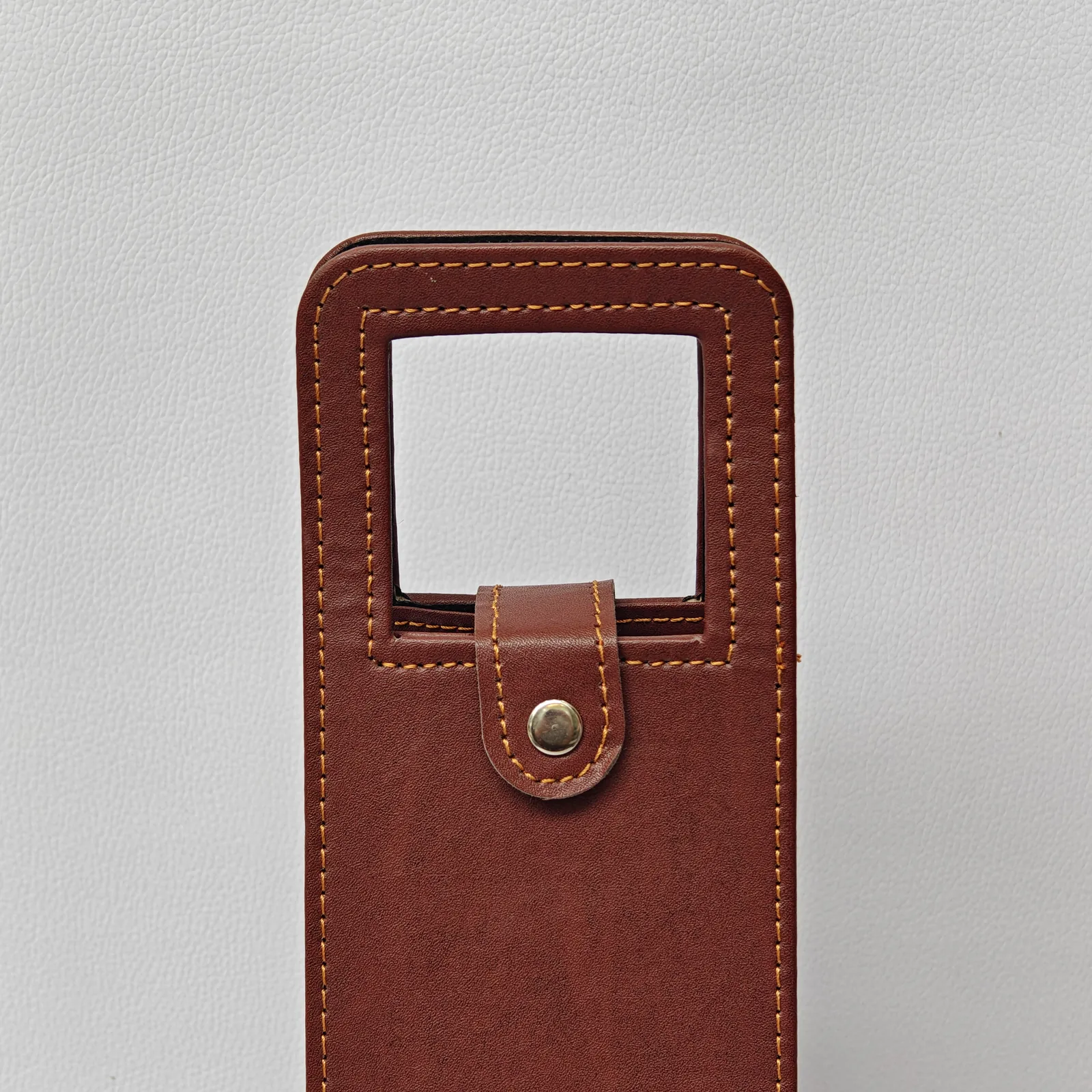 Close-up of the integrated handle and snap button closure on a brown leather wine carrier.