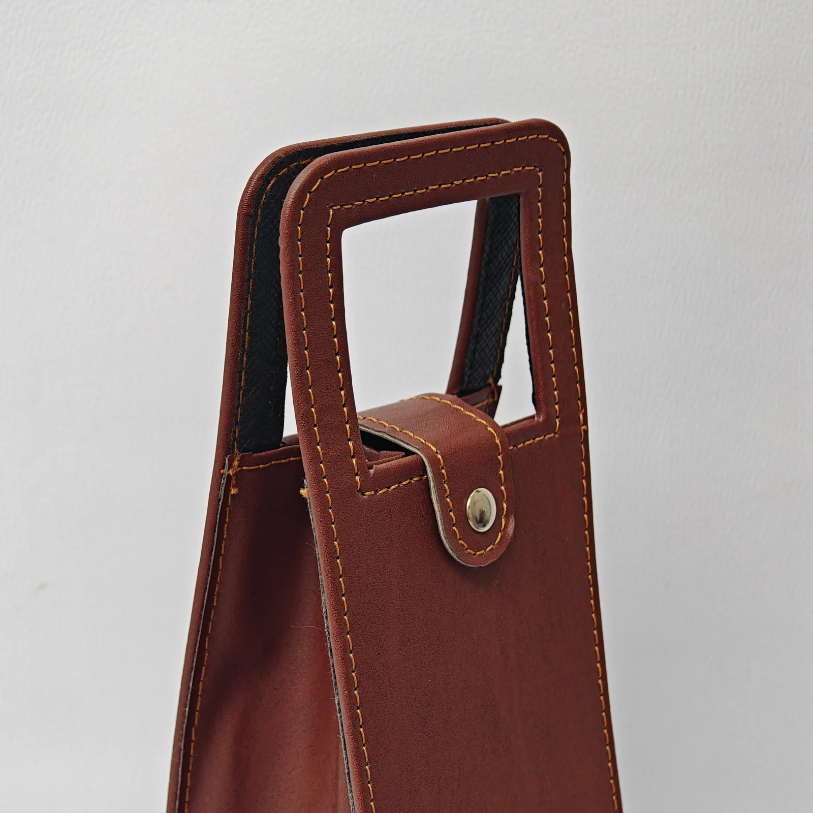 Detail view of the snap closure and handle on a brown leather wine carrier.