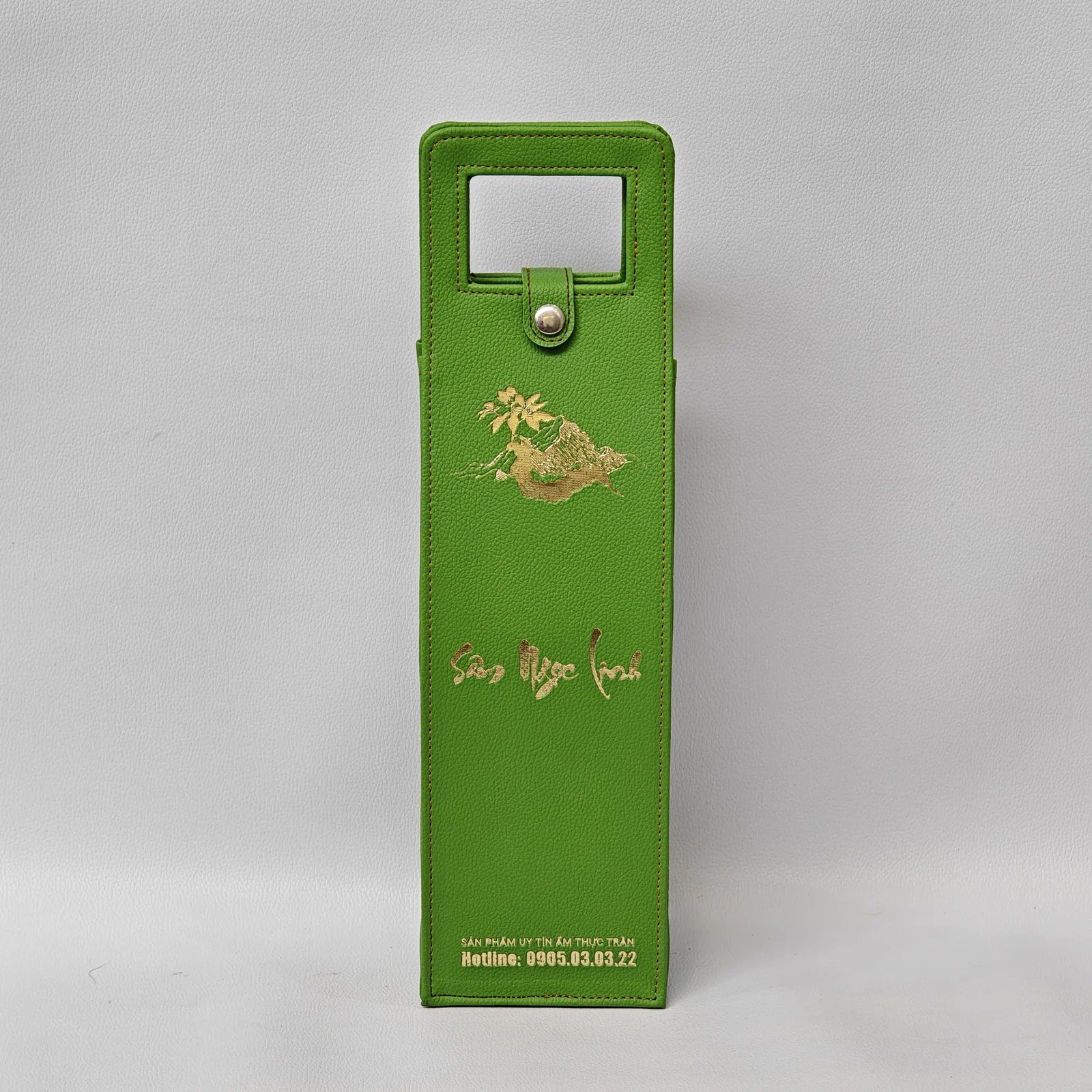 Front view of a green pebbled leather wine carrier with gold foil logo and text.