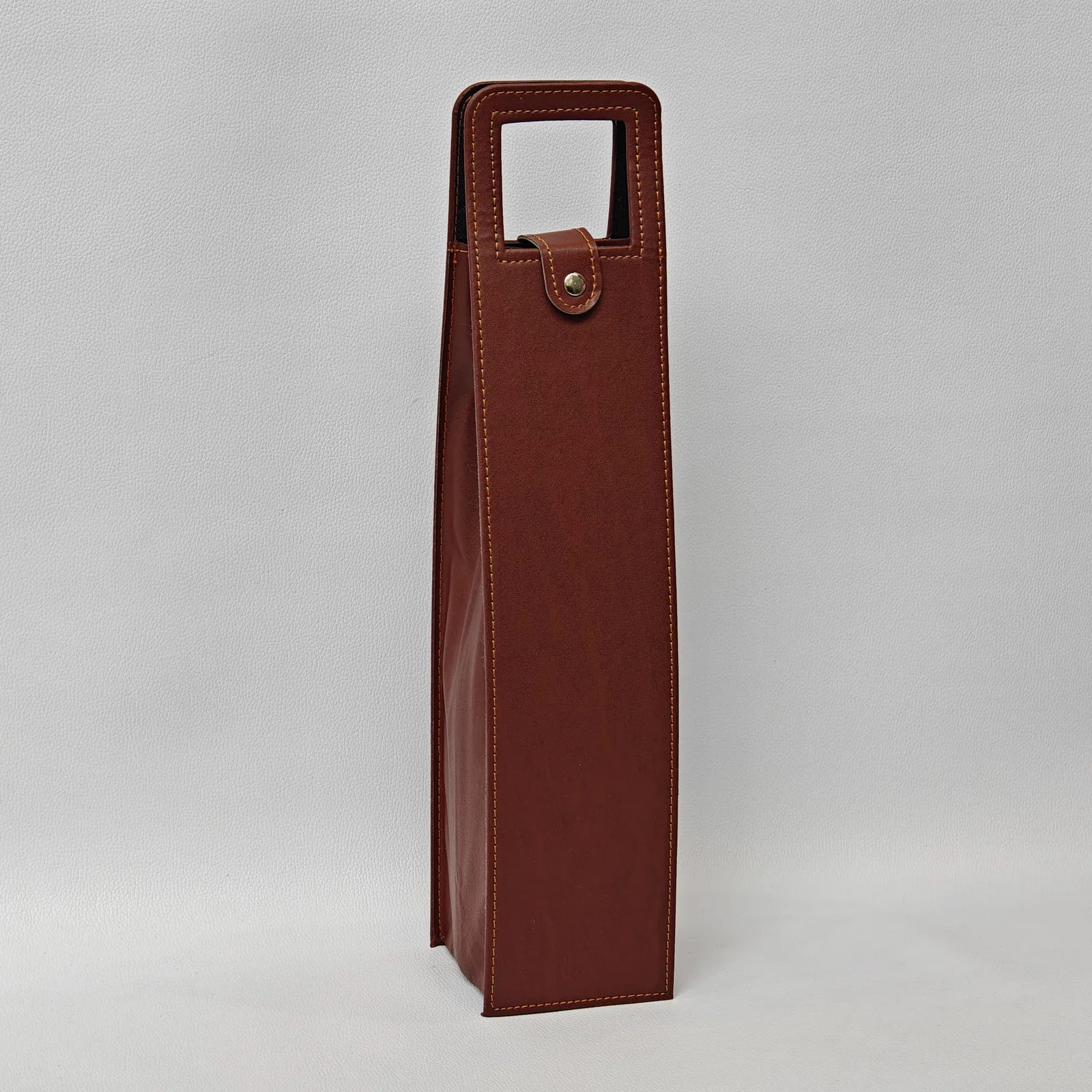 Angled view of a brown leather wine bottle carrier with contrast stitching and a snap closure.