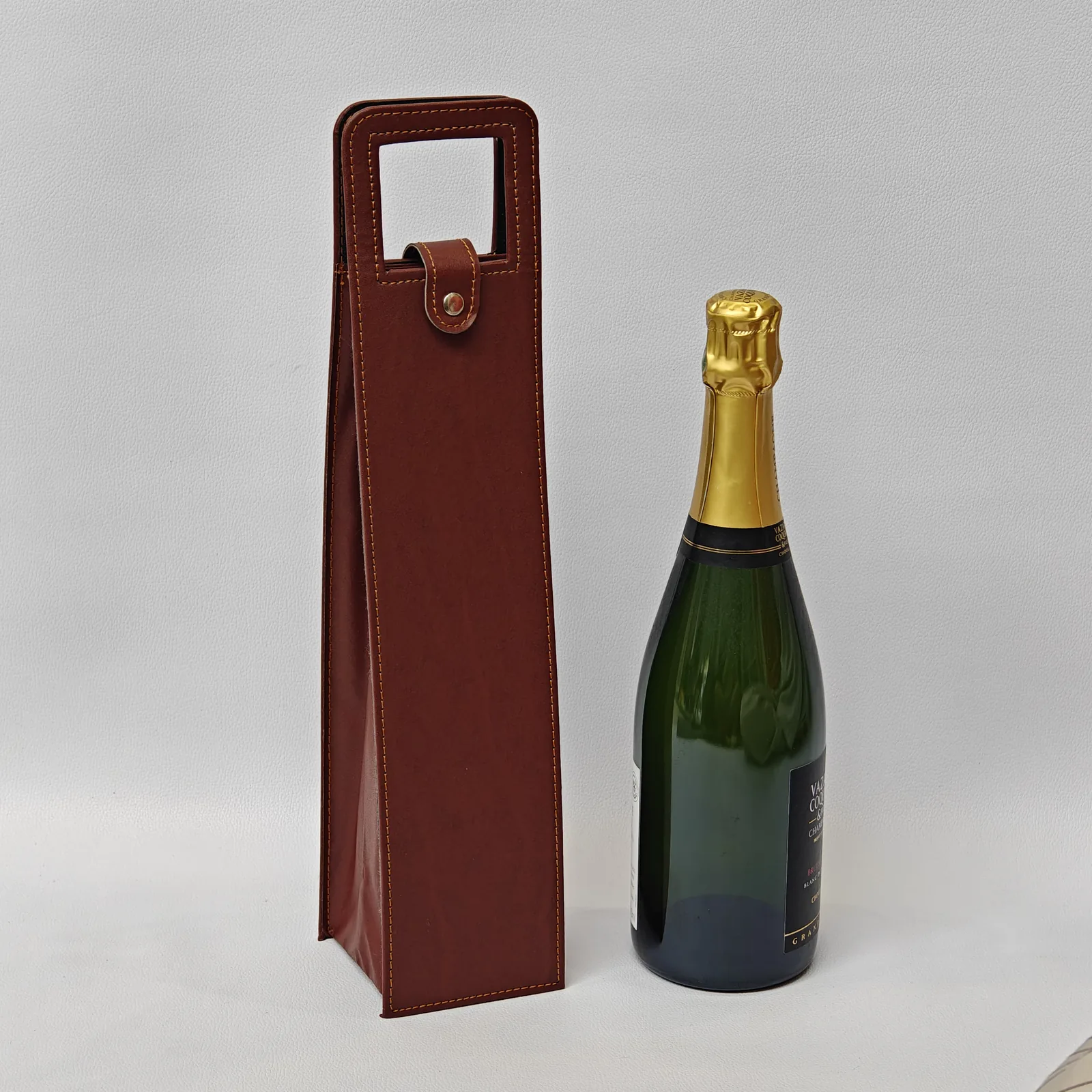 Brown leather wine carrier standing next to a champagne bottle for scale.