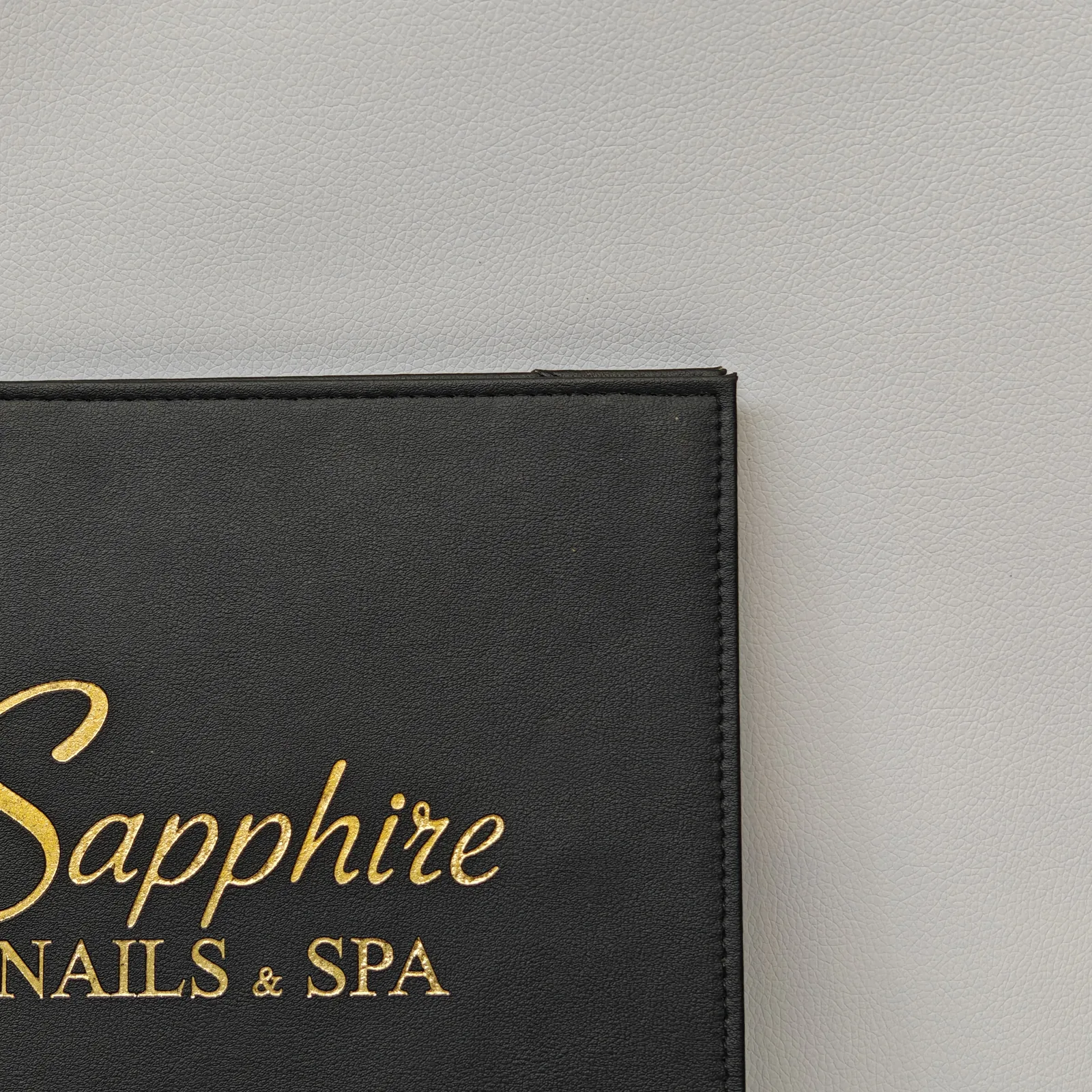 Close-up of gold foil text and corner stitching on a black pebbled leather cover.