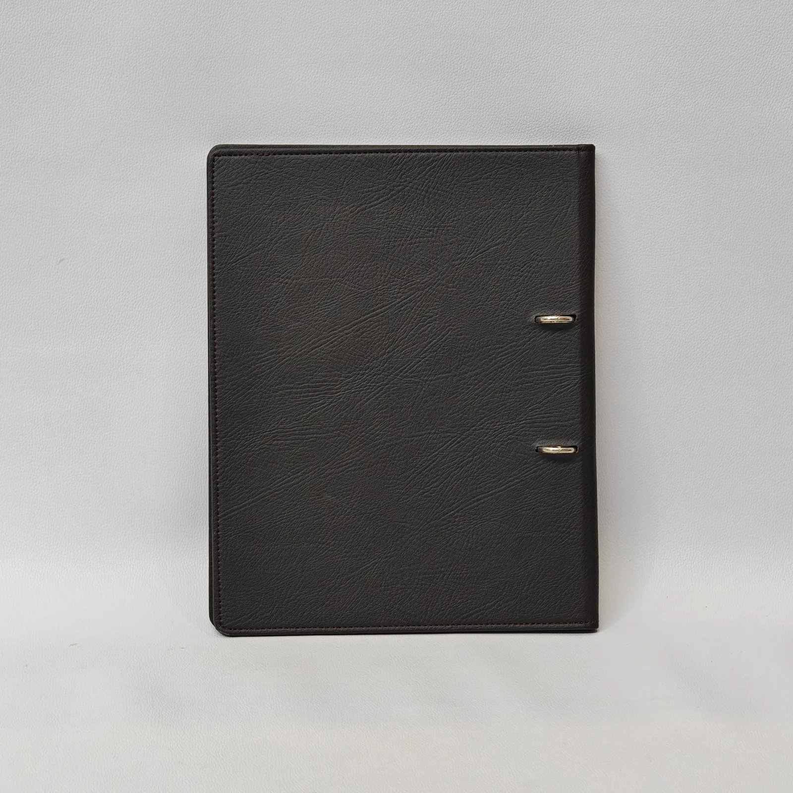 Back view of a dark brown leather binder showing silver rings through two horizontal slots.