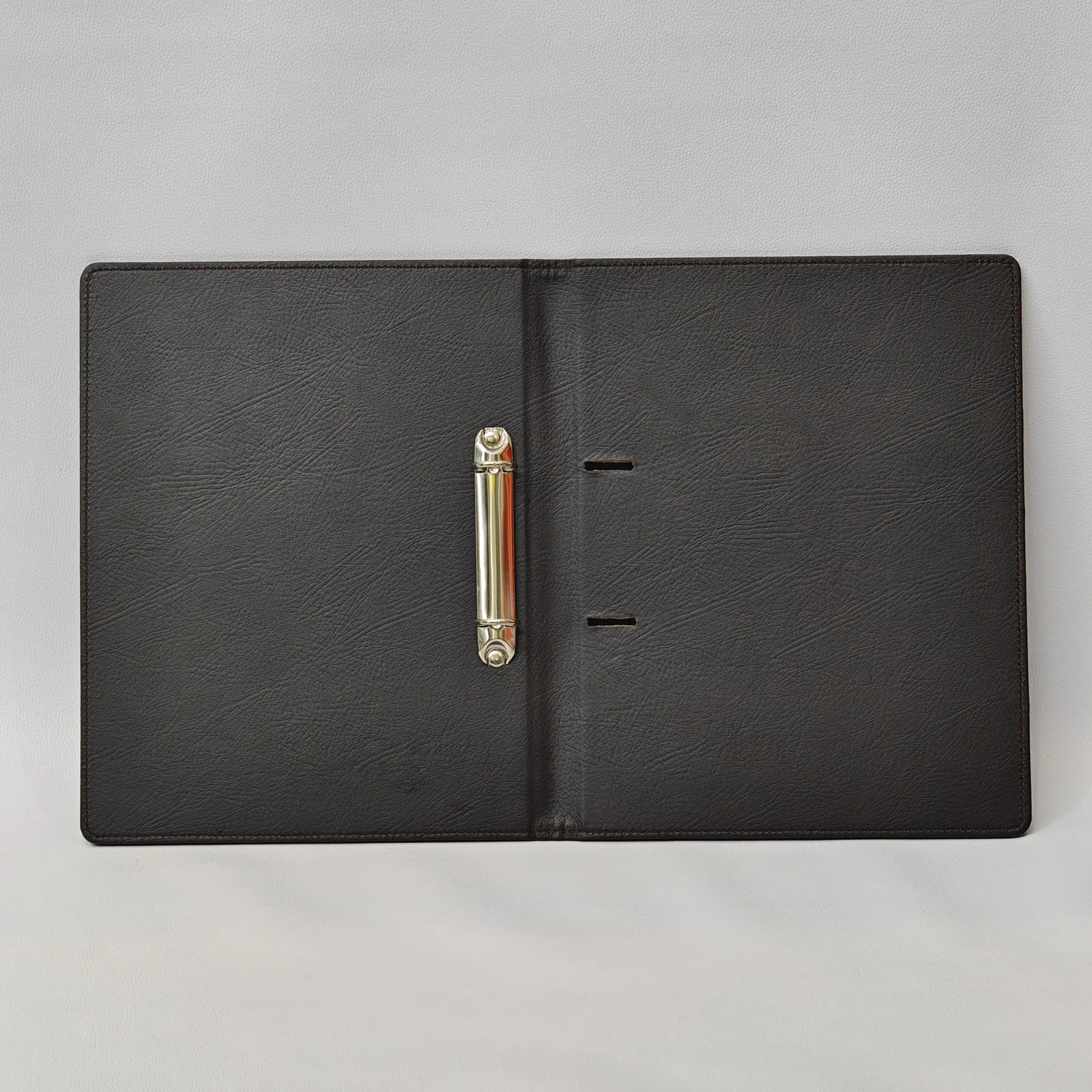 Interior view of an open dark brown leather binder with a silver two-ring mechanism.