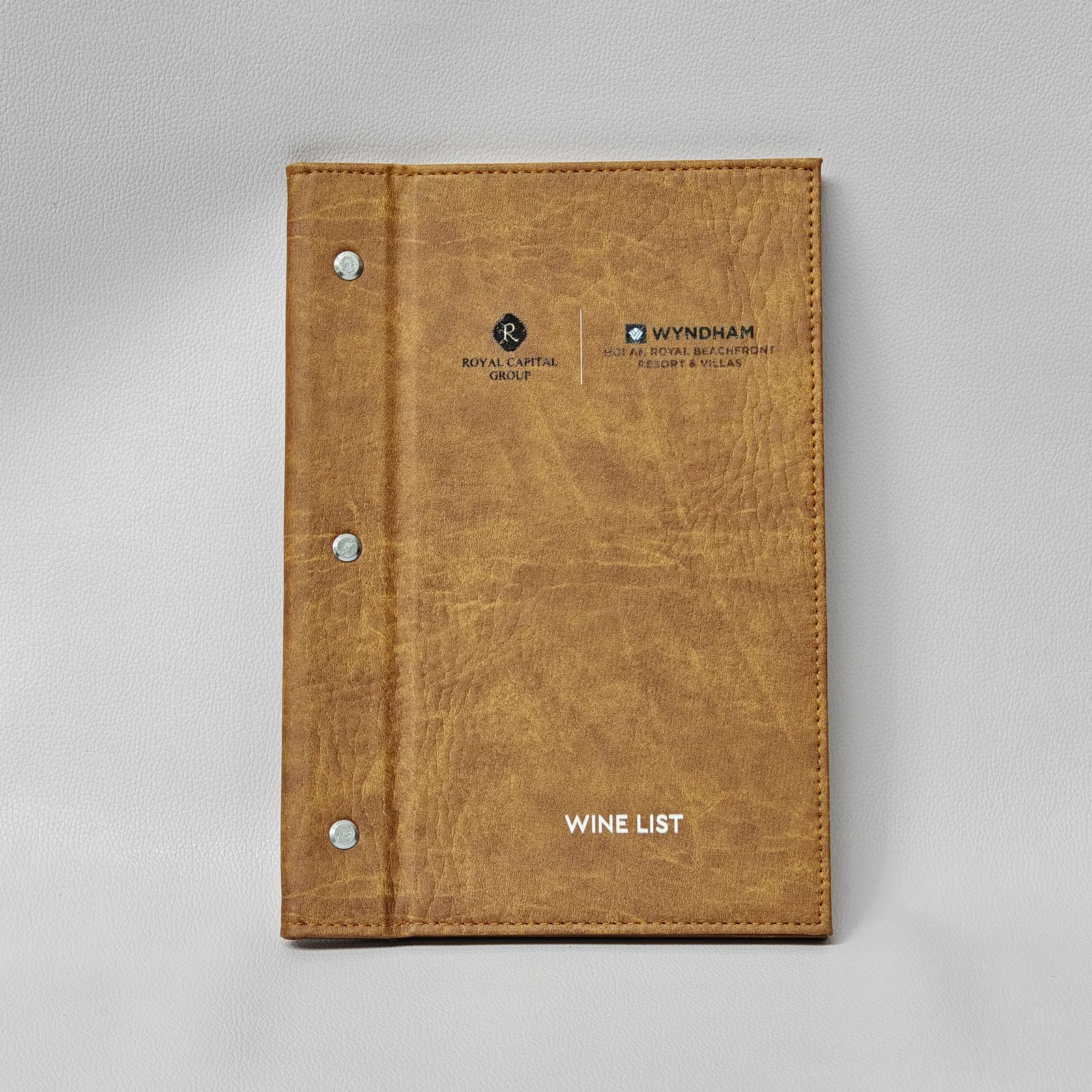 Tan leather wine list cover with metal snap closures and embossed branding