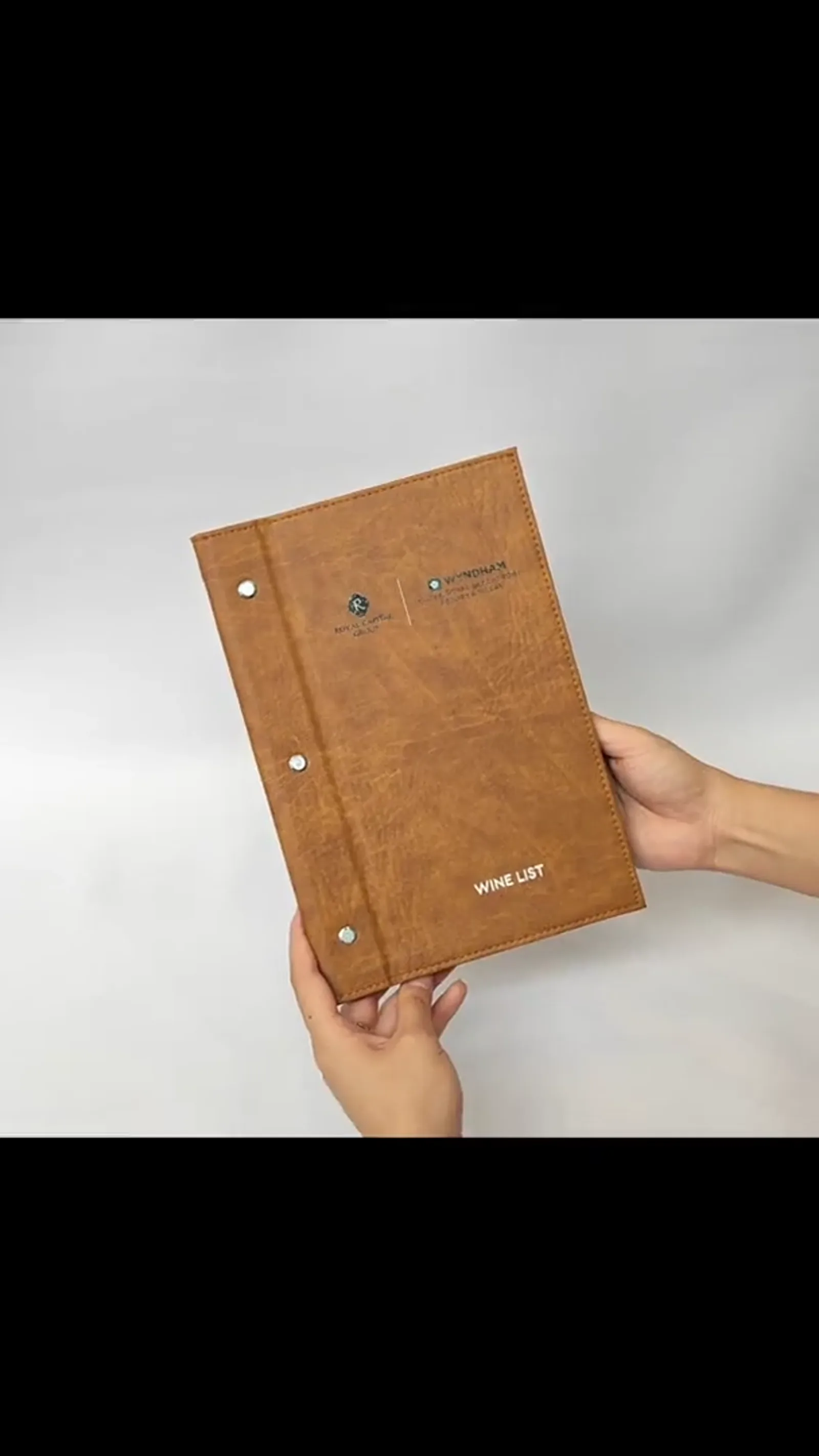 Hands holding open wine list binder with interior pages visible