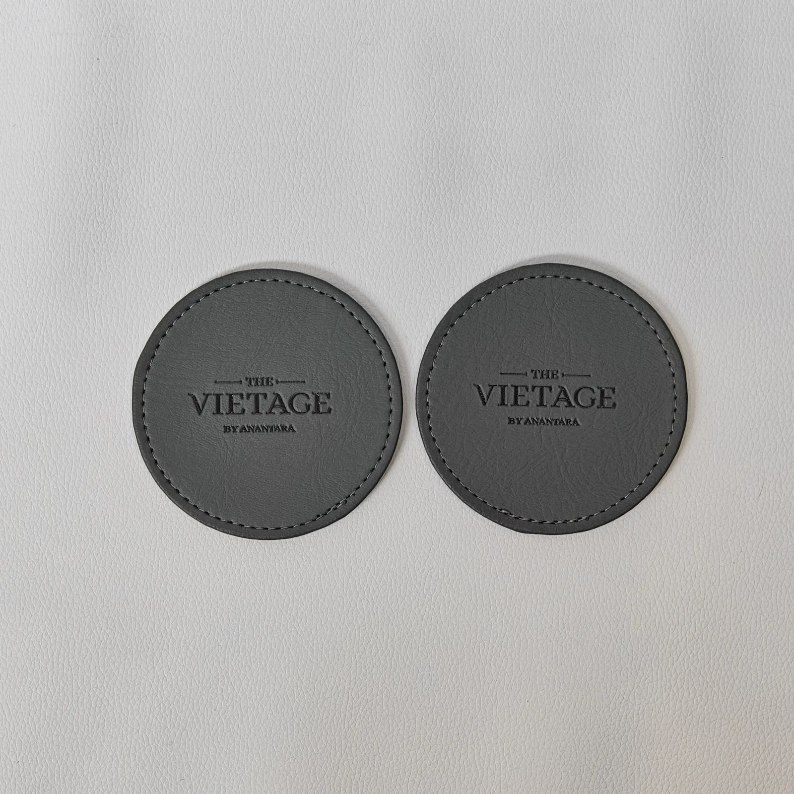 Pair of round gray leather coasters with embossed branding and stitched edges
