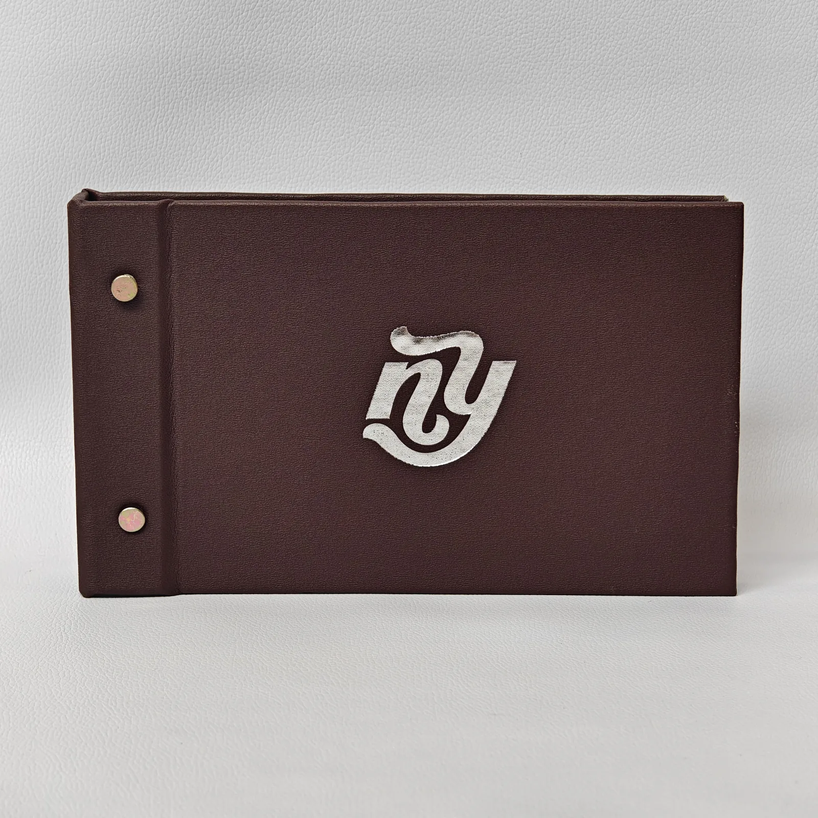 Dark brown textured landscape menu cover with two screw posts on the left and a silver logo in the center.