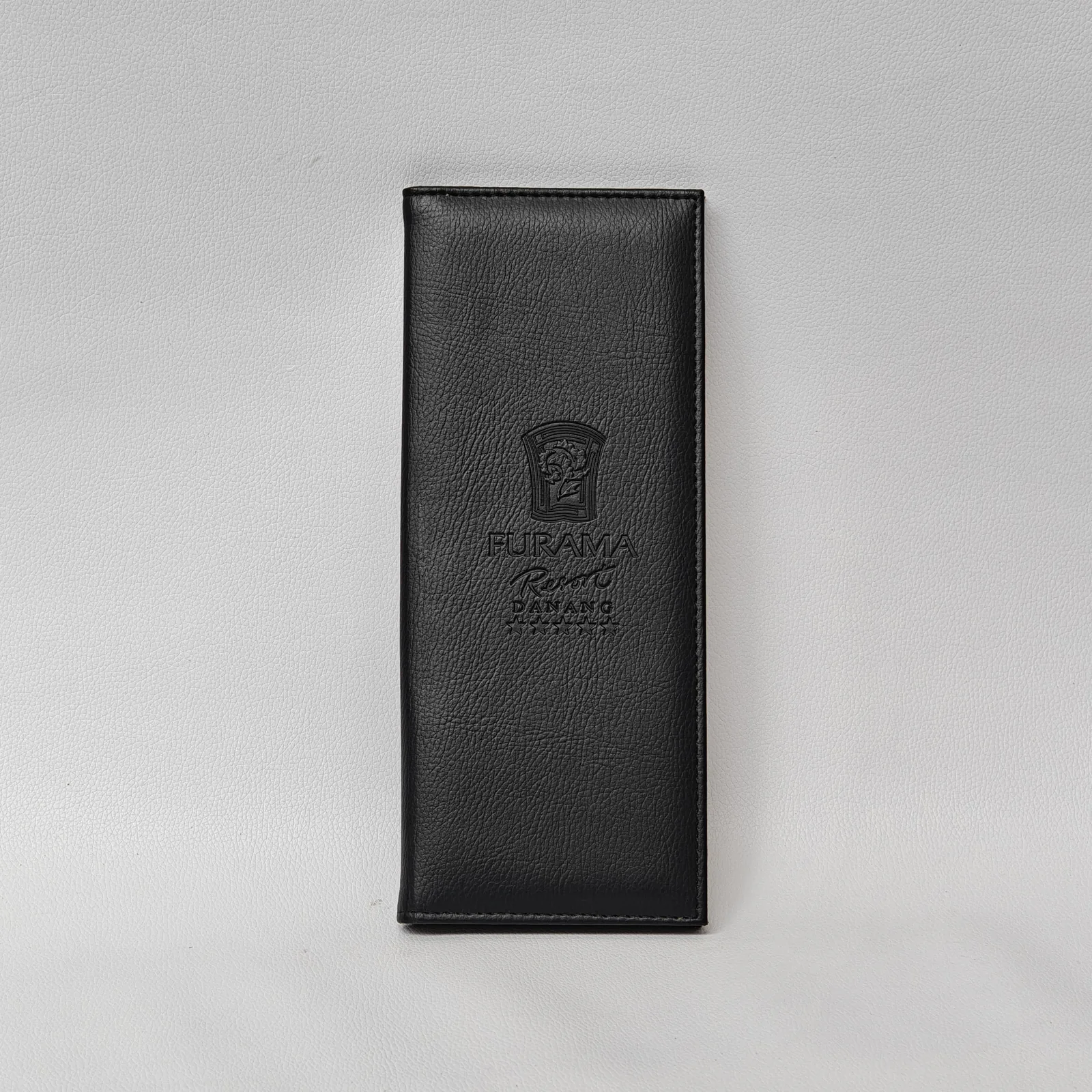 Front view of a closed black leather check presenter with an embossed logo and perimeter stitching.