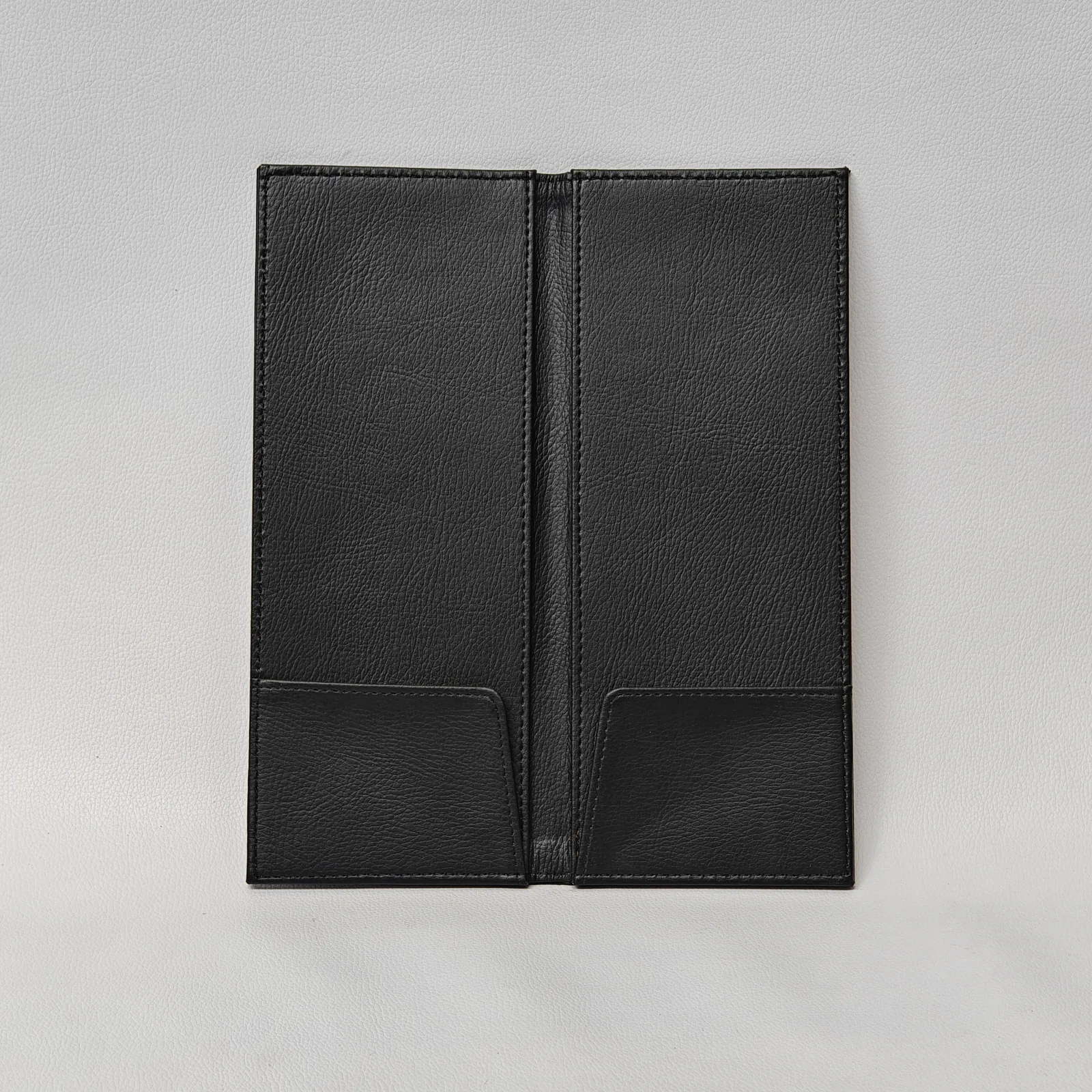 Interior view of an open black leather check presenter showing two bottom pockets and a central fold.