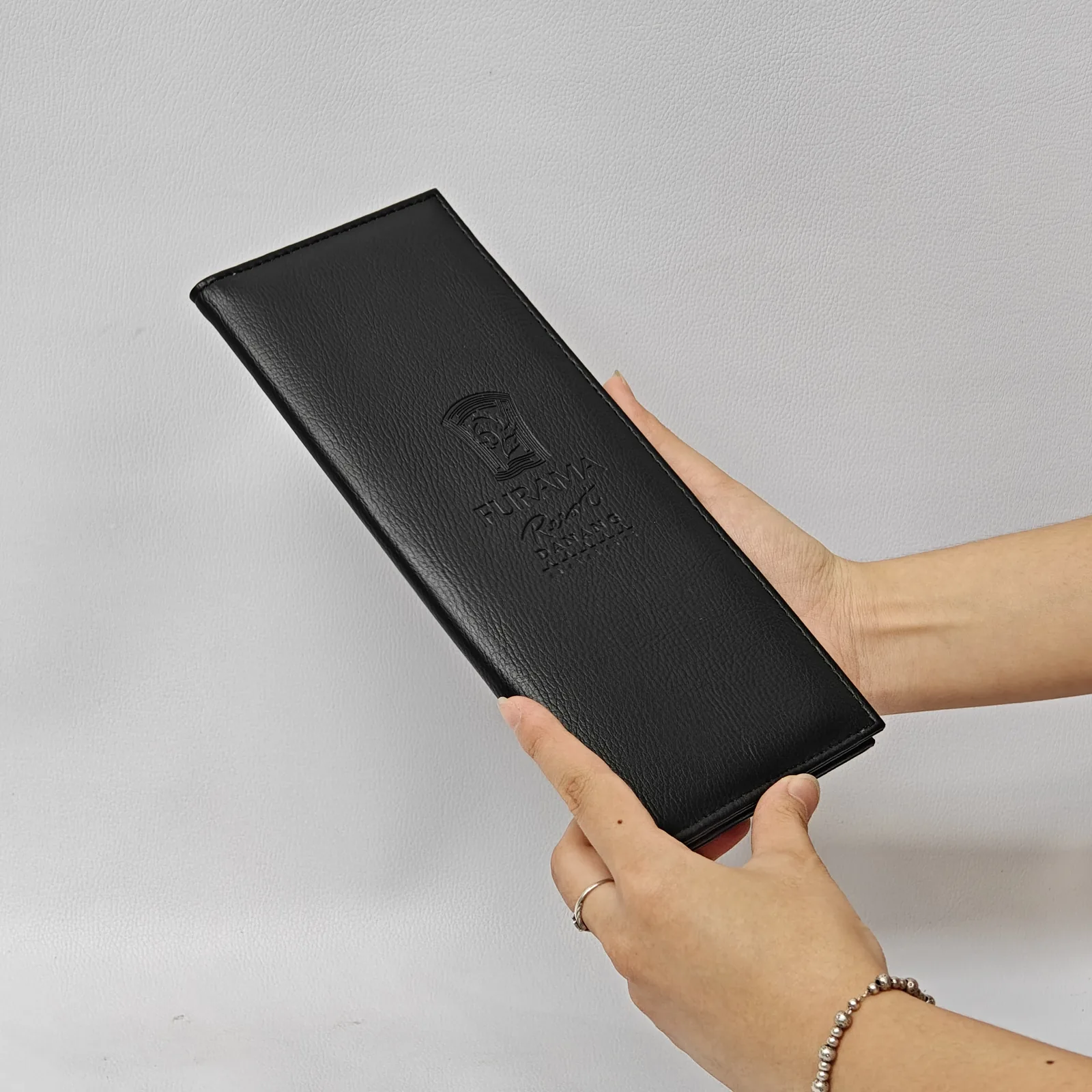A person holding a black leather check presenter at an angle, showing its size and textured surface.