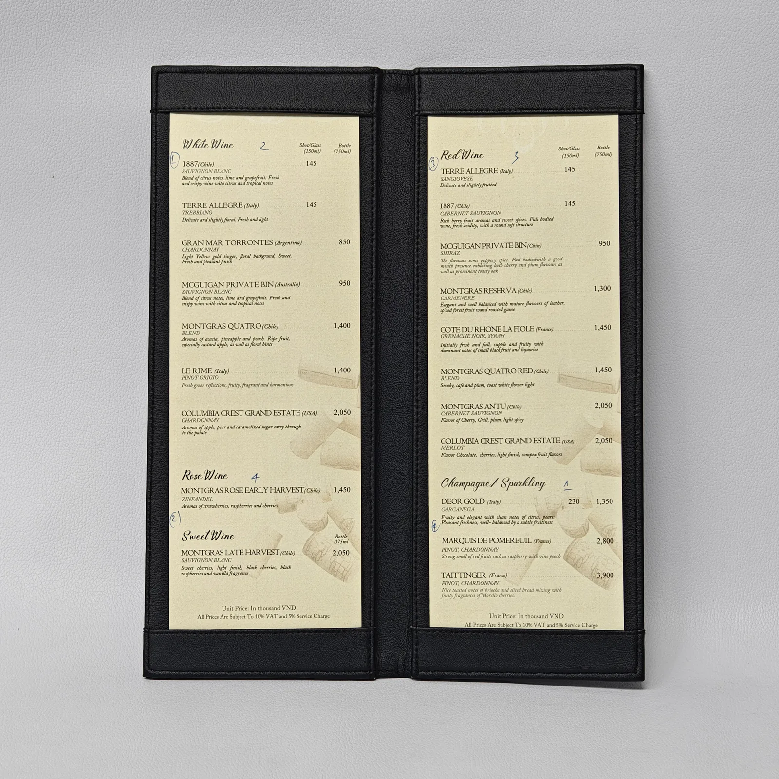Open black leather menu cover displaying a wine list held in place by top and bottom leather bands.
