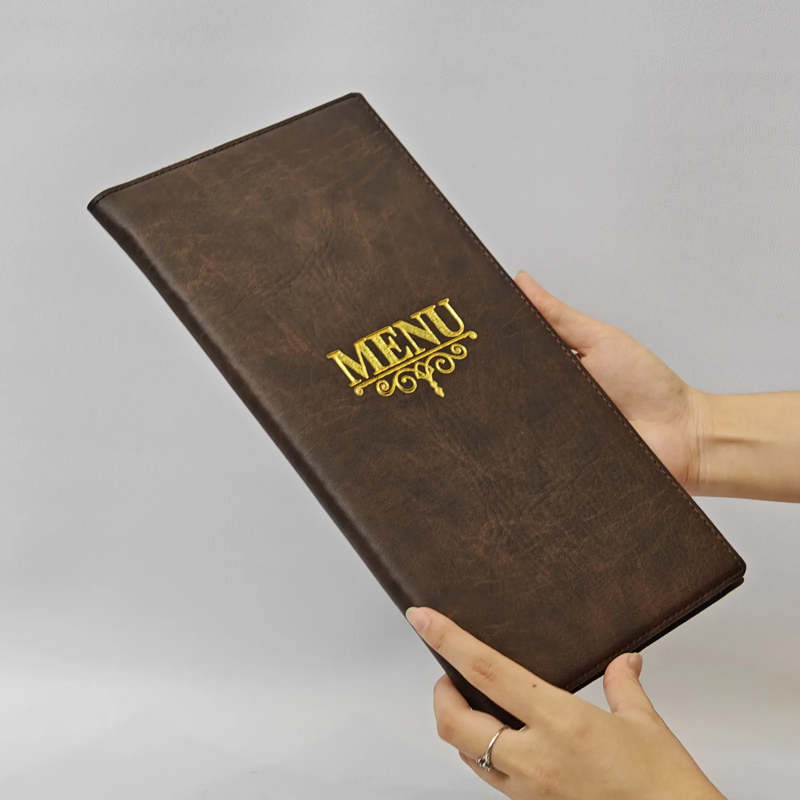 A person holding the closed brown leather menu cover.